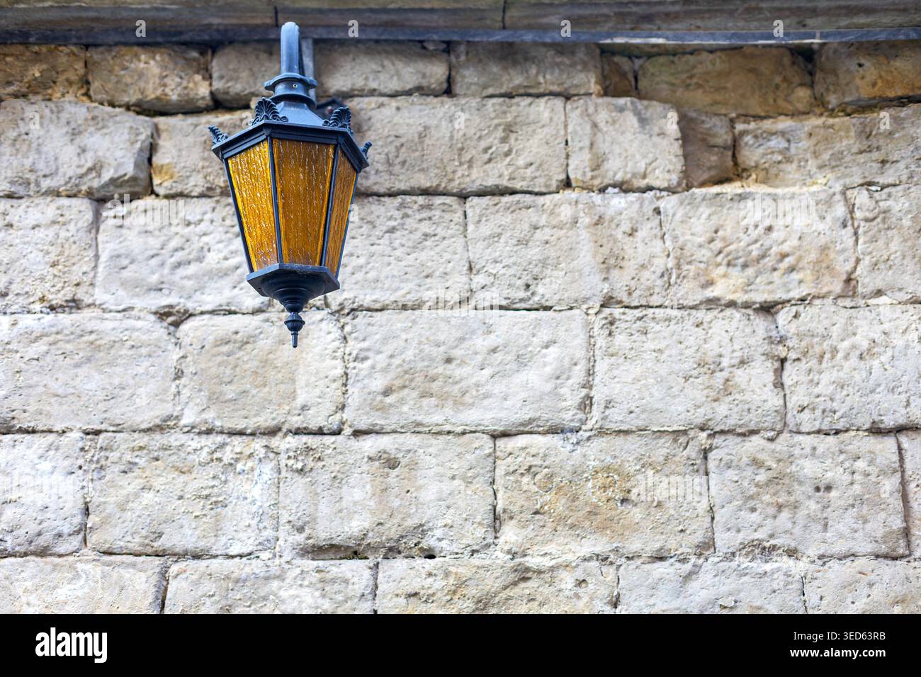 Lanterne vintage sur mur de pierre. Lanterne suspendue à l'ancienne avec verre ambré monté contre un mur de pierre altérée, créant une architecture rustique Banque D'Images