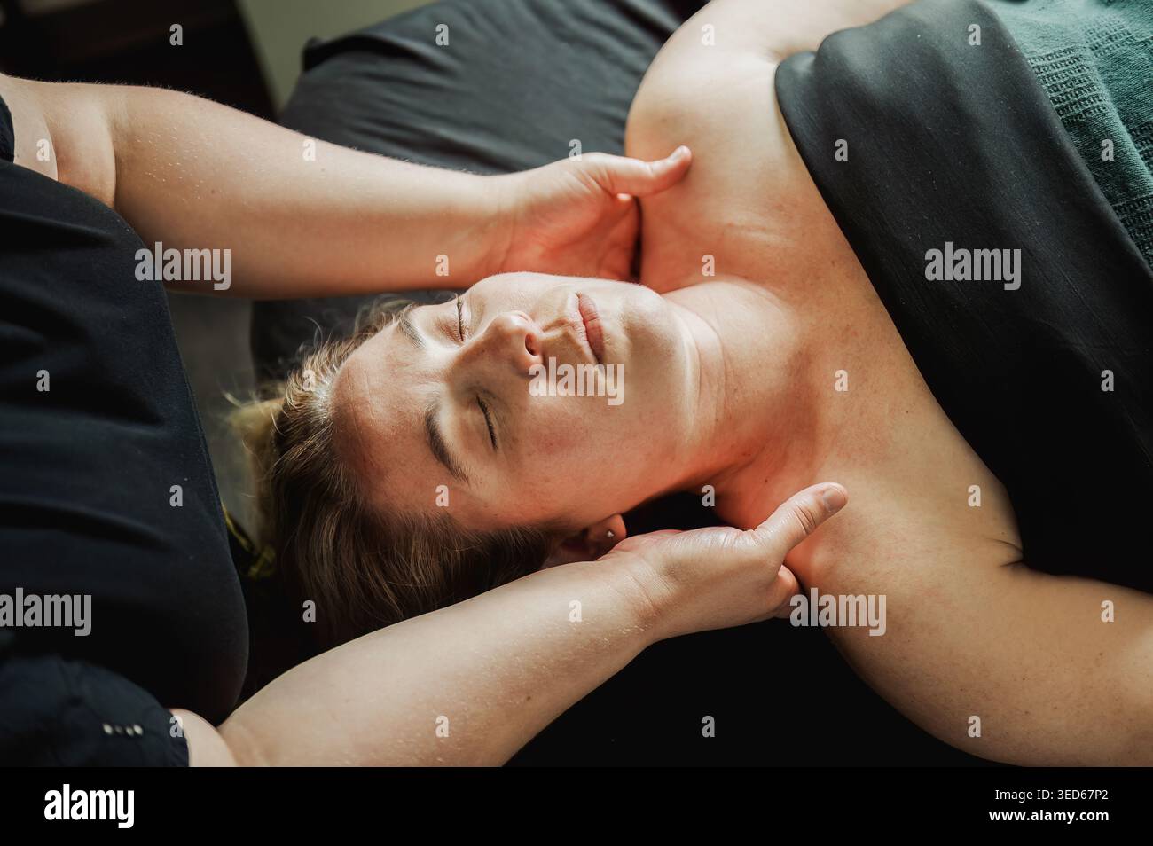 Femme recevant un massage du cou et de l'épaule, les yeux fermés, lumière chaude Banque D'Images