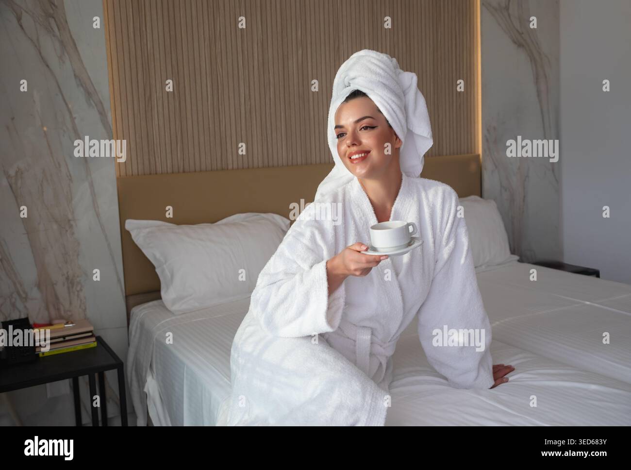 Belle femme assise sur le lit tenant le café. Portrait doux avec serviette sur la tête. Ambiance matinale calme dans la chambre d'hôtel. Concept de style de vie relaxant du spa. Peau Banque D'Images