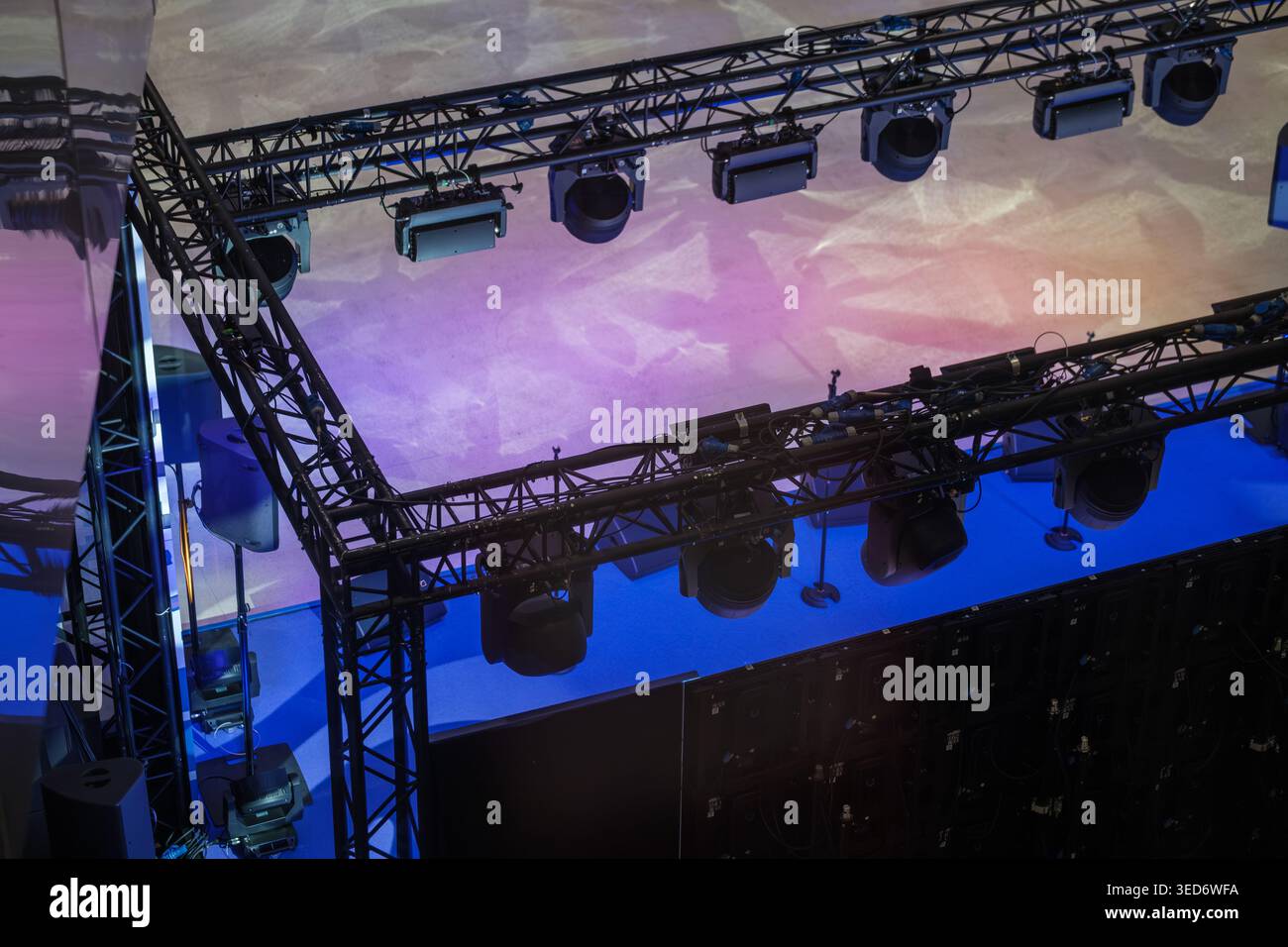 Éclairage de scène suspendu et système de treillis projetant des lavages violets et bleus, des projecteurs et du gréement pour la production de concerts, la mise en scène d'événements et la configuration de spectacles en direct. Banque D'Images