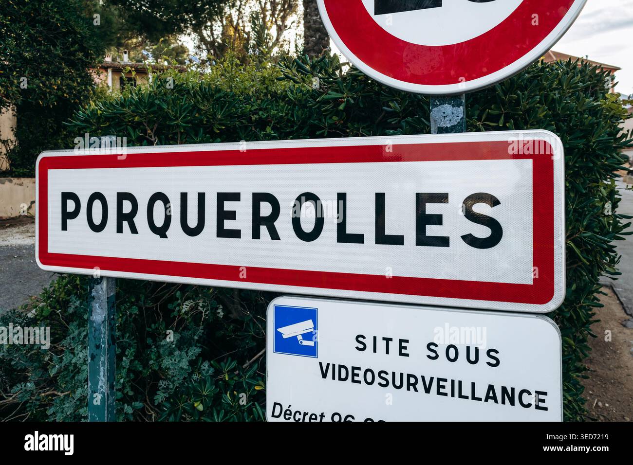Porquerolles, France - 7 décembre 2025 : panneau d'entrée du village de Porquerolles avec limite de vitesse et avis de surveillance, palmiers et Méditerranée Banque D'Images
