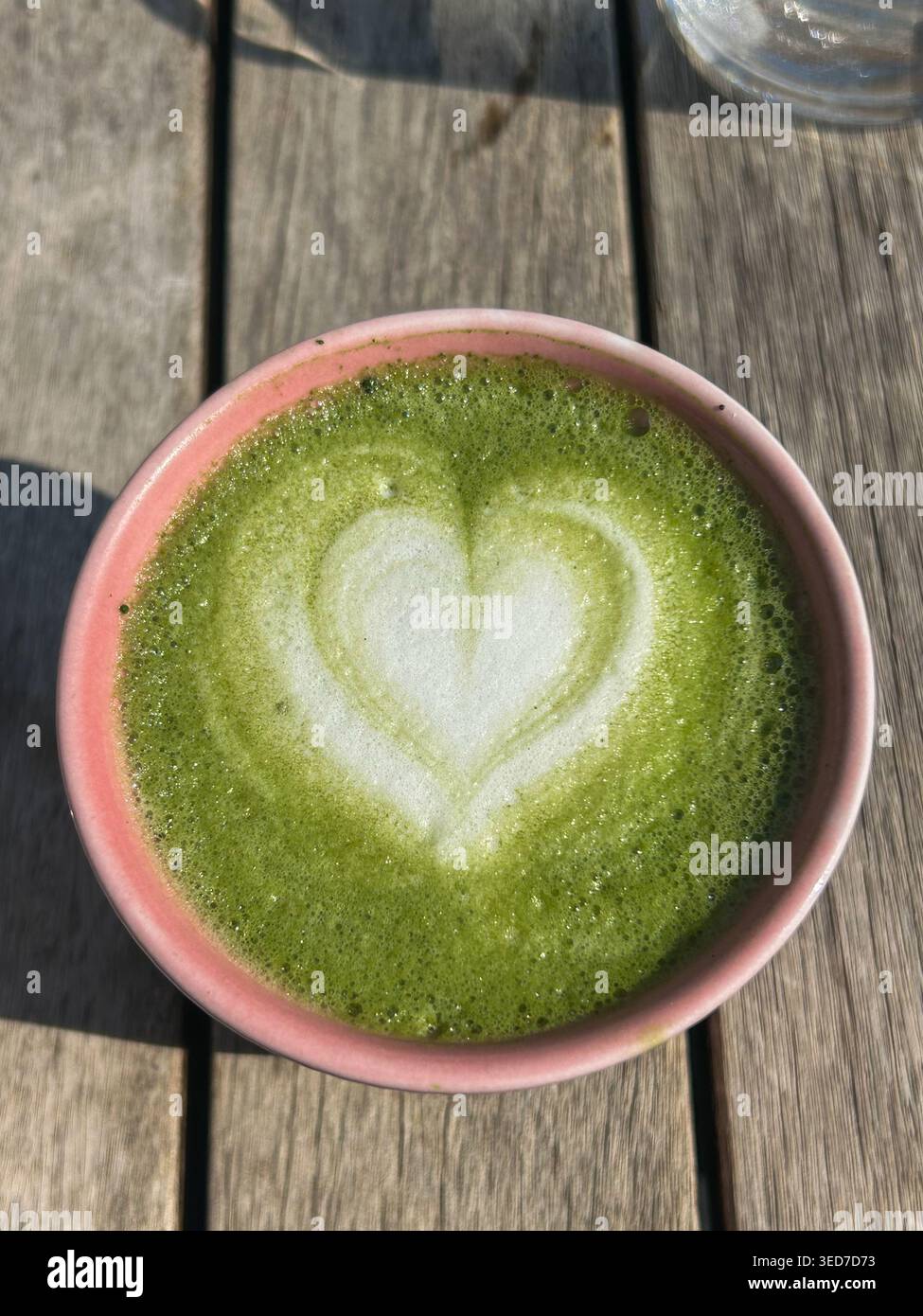 Vue de dessus de matcha latte avec art en mousse en forme de coeur dans une tasse en céramique sur une table en bois à la lumière naturelle du soleil. Banque D'Images