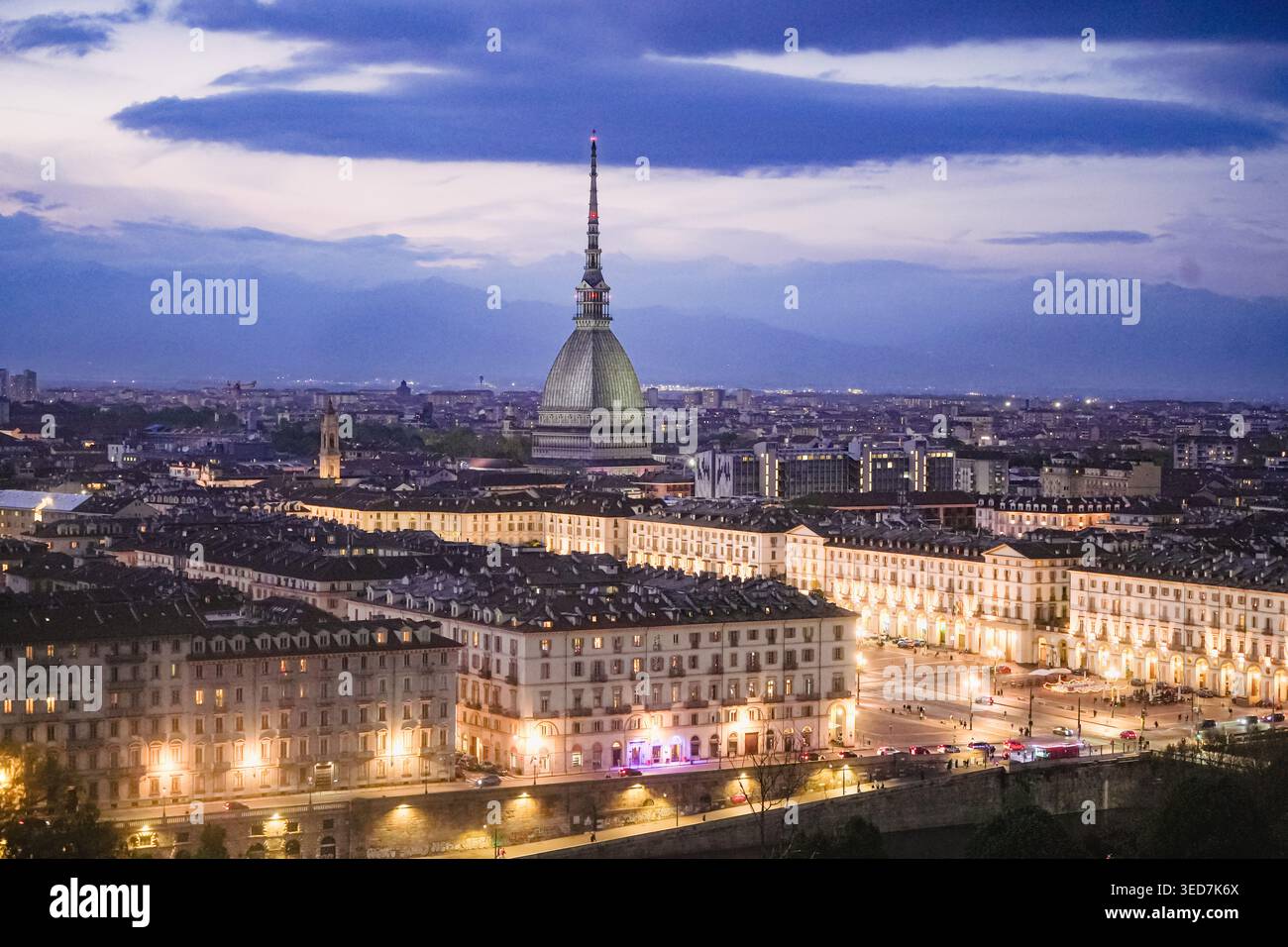 Vue aérienne de la mole Antonelliana et la ligne d'horizon illuminée de la ville avec les Alpes en arrière-plan au crépuscule à Turin, Piémont, Italie. Banque D'Images