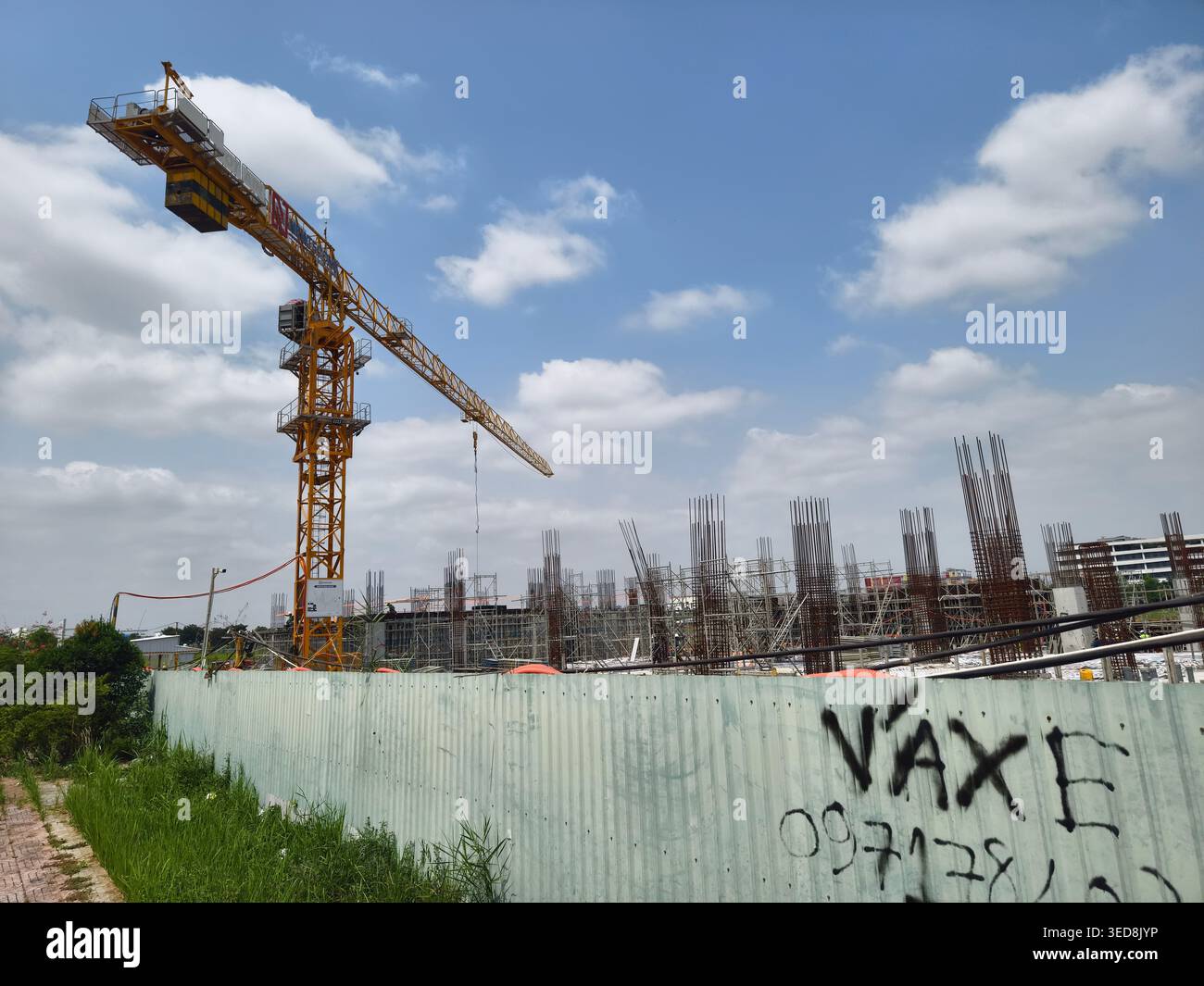Grue à tour jaune installée sur un chantier de construction avec des colonnes de ferraillage exposées derrière une clôture en tôle ondulée, développement du parc high-tech de Saïgon Banque D'Images