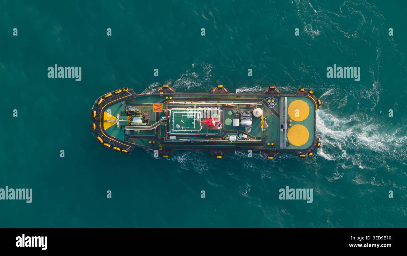 Vue aérienne d'un remorqueur naviguant dans les eaux turquoises avec un sillage blanc près du port de Laem Chabang, Chon Buri, Thaïlande. Banque D'Images