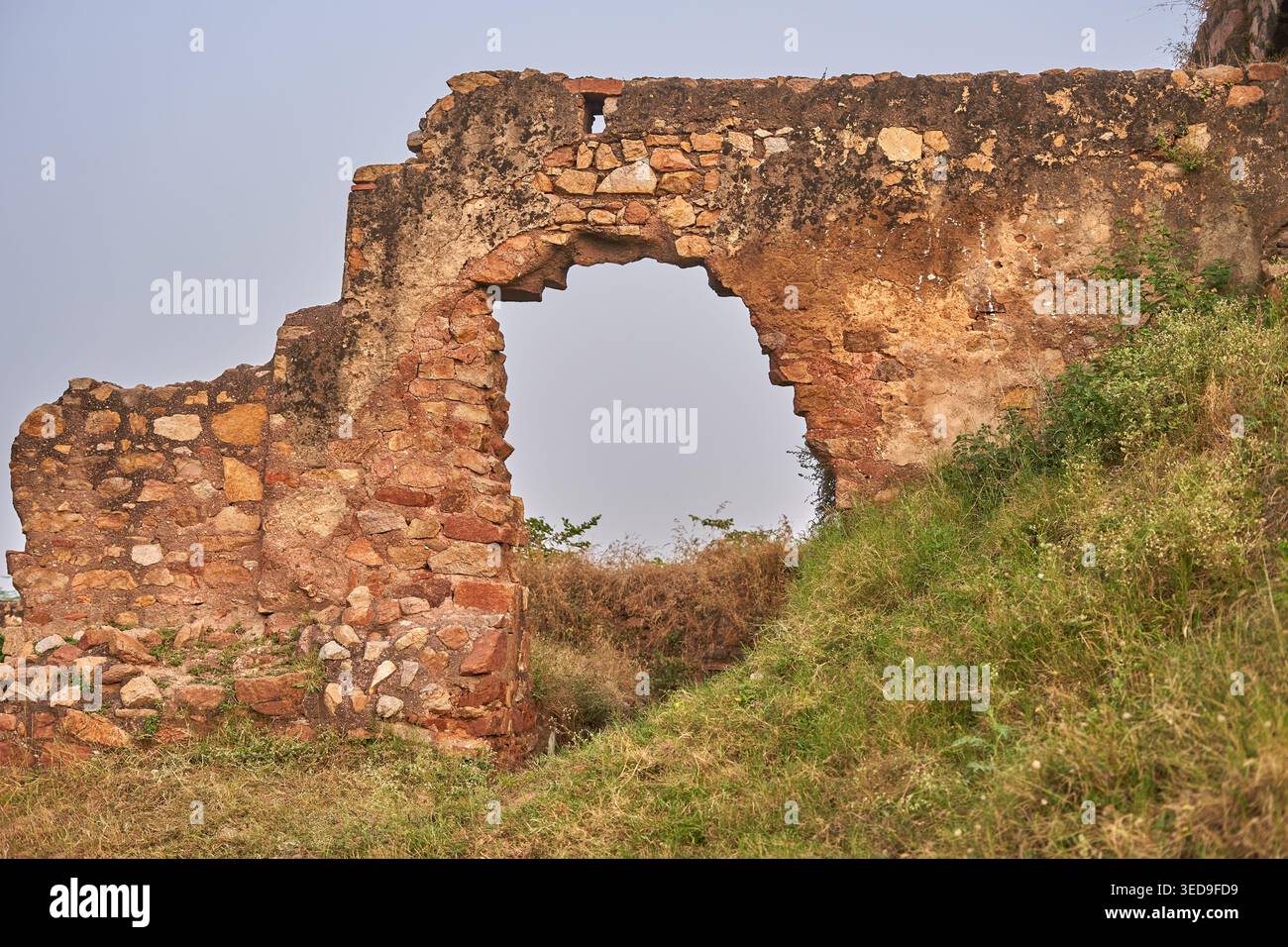 Ruines anciennes en pierre érodées présentant une grande ouverture en arc construite à partir de pierres irrégulières dans des tons bruns, rouges et beiges. La détériorée Banque D'Images
