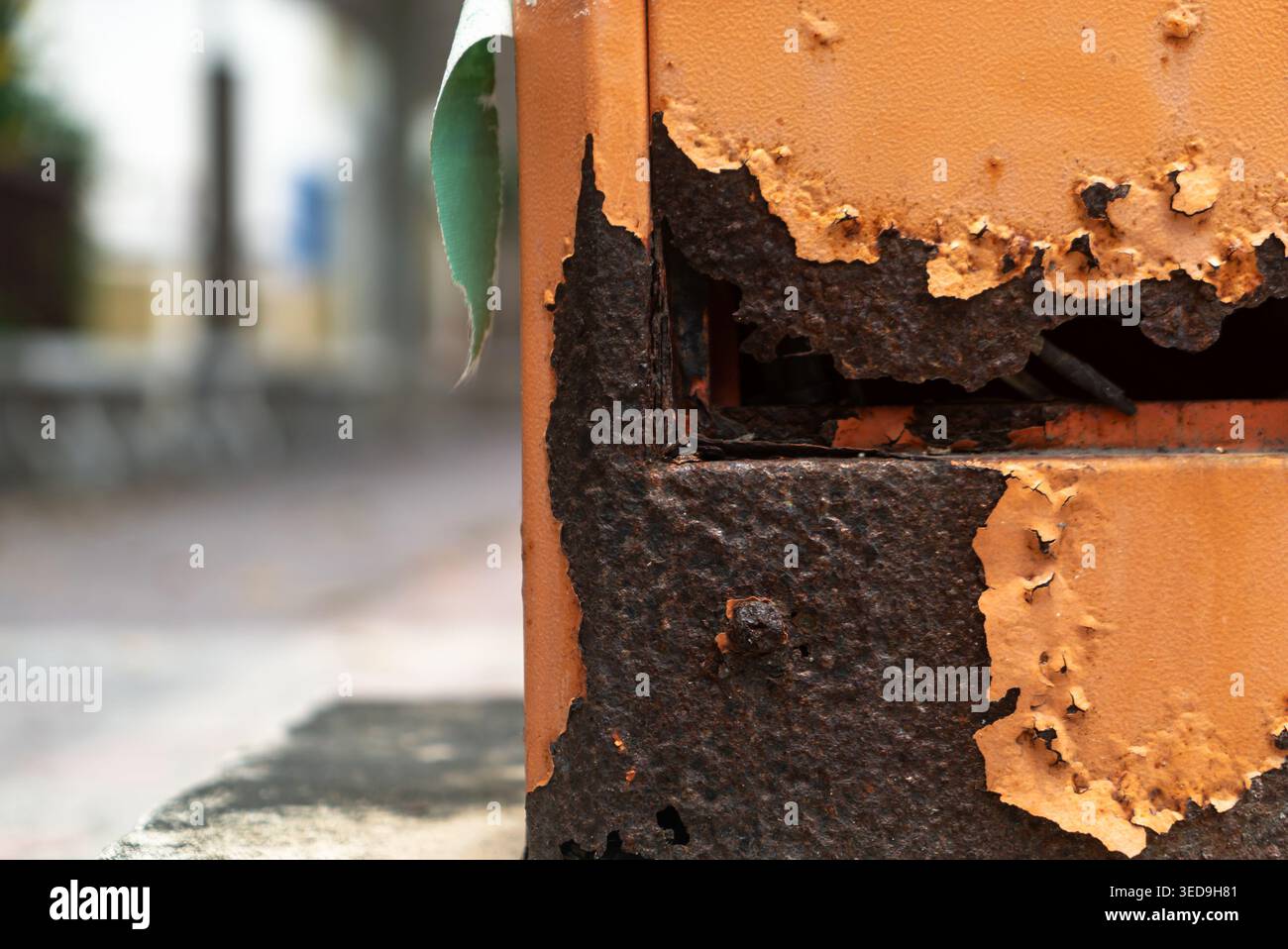 Cette photographie en gros plan capture un mur altéré avec une peinture orange écaillée et une base noire et corrodée, mettant en évidence les textures de la décomposition et de l'extérieur Banque D'Images