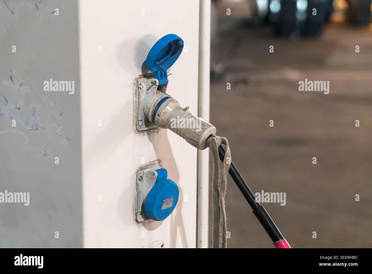 Gros plan d'une prise de courant avec une brosse de nettoyage suspendue à celle-ci, dans un environnement industriel. Met en évidence la maintenance électrique et le nettoyage pro Banque D'Images