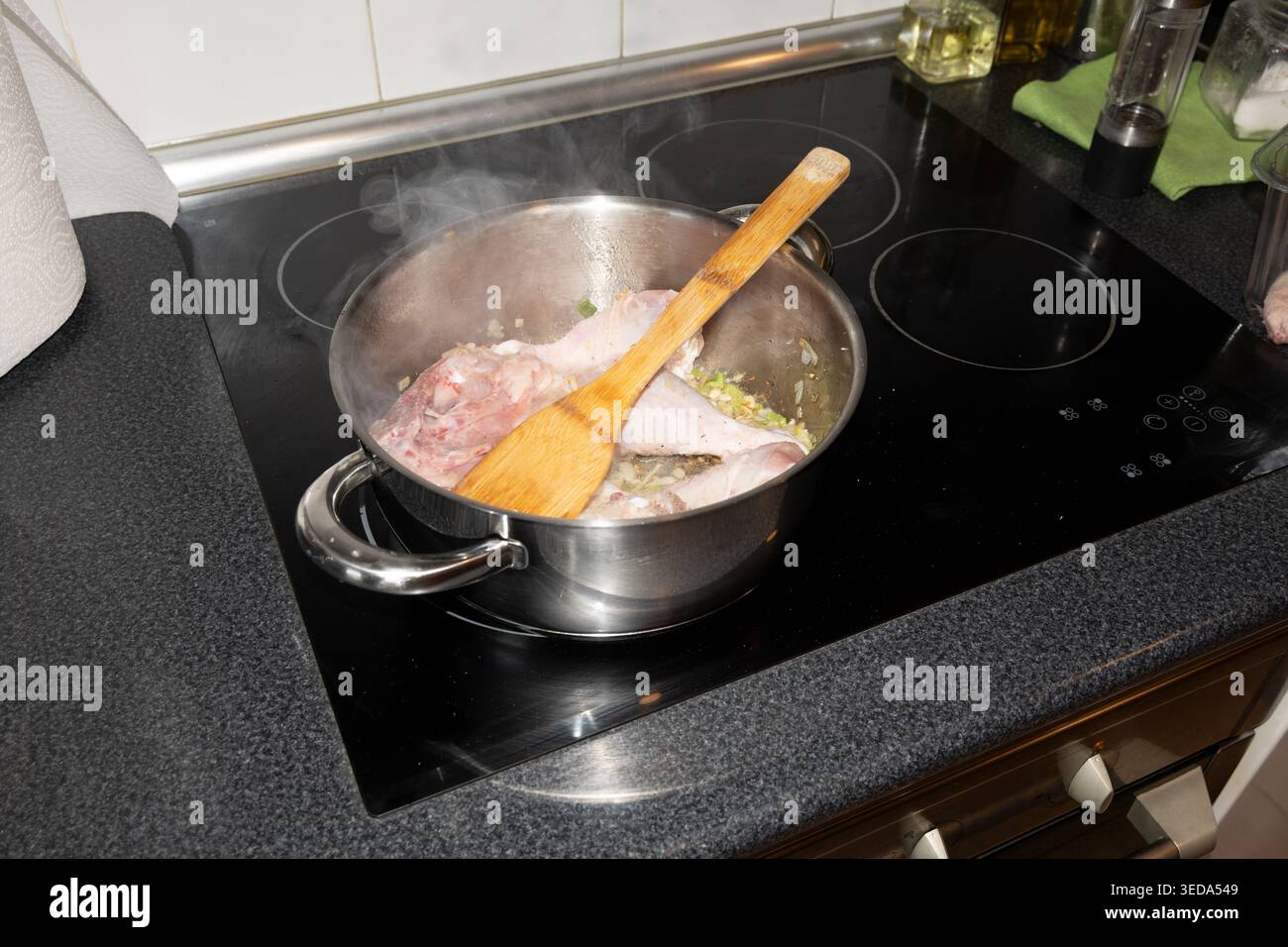 Morceaux de volaille et légumes mijotant dans une casserole en acier avec une cuillère en bois sur une table de cuisson à induction Banque D'Images