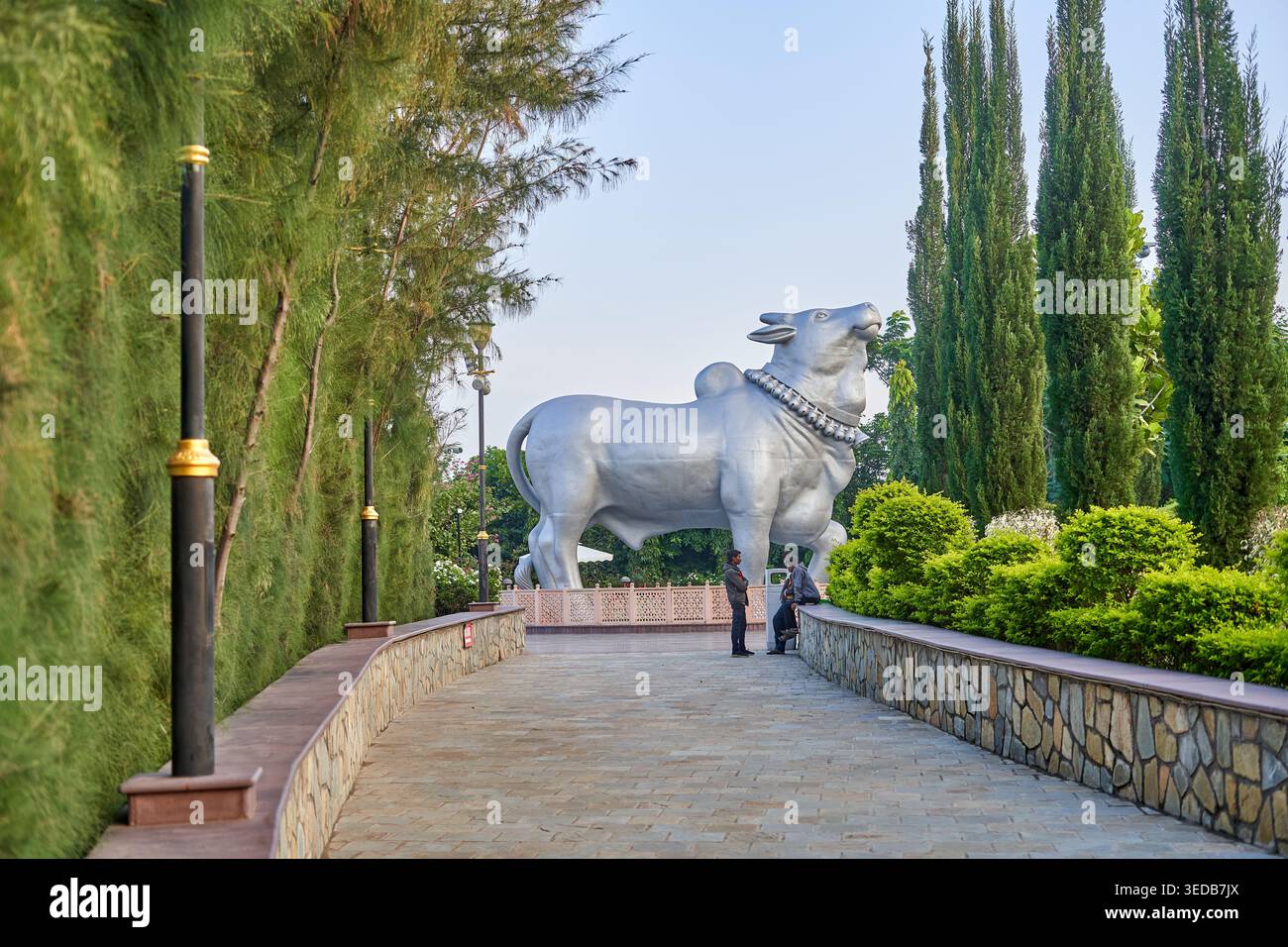 Une grande statue argentée de Nandi, le taureau sacré dans la mythologie hindoue, se dresse de manière proéminente au bout d'une allée pavée. La sculpture présente Banque D'Images