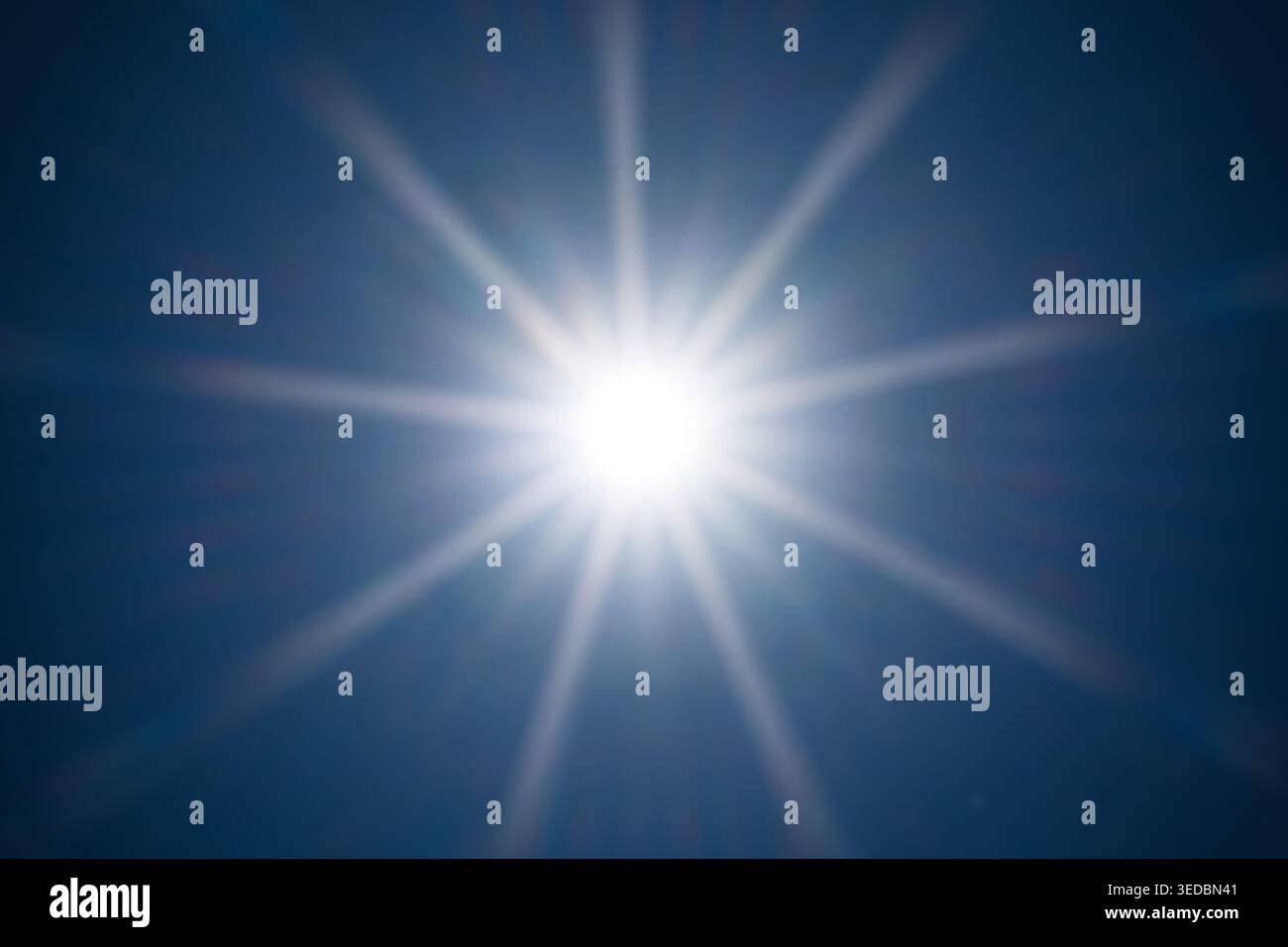 Une étoile de soleil symétrique brille brillamment au centre d'un ciel bleu foncé. La composition propre met en évidence les rayons de lumière naturelle et les rayons du soleil Banque D'Images