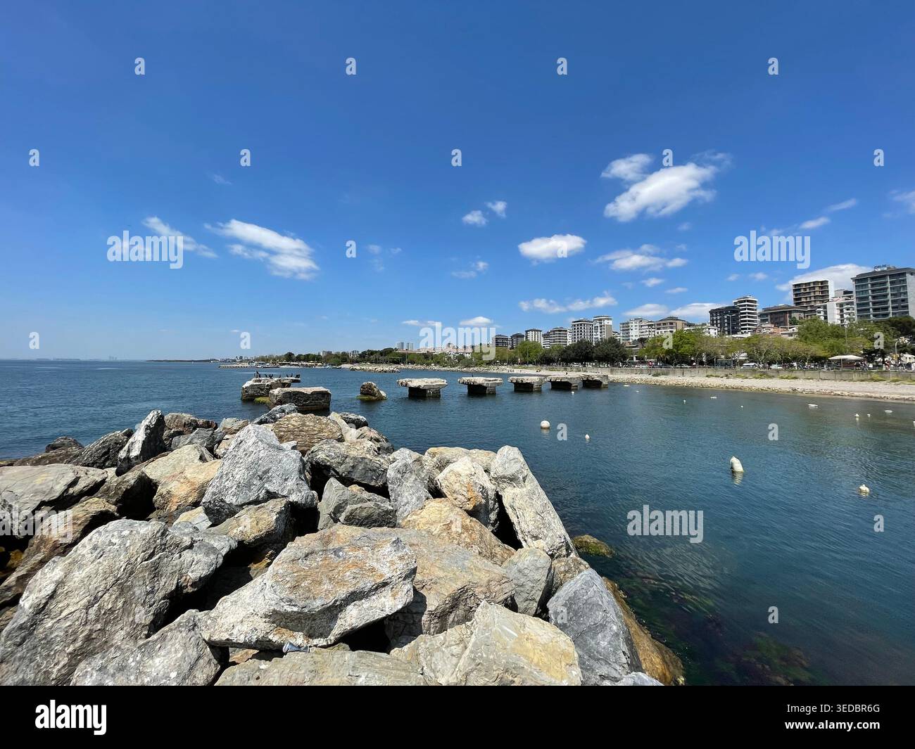 Scène côtière avec de grands rochers au premier plan et une mer calme menant à une ligne d'horizon urbaine lointaine. Banque D'Images