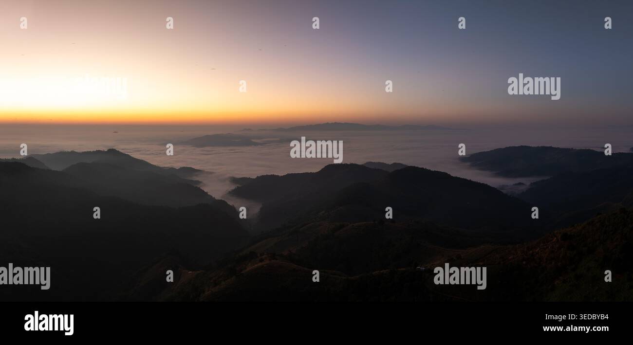 vue panoramique de crêtes montagneuses silhouettées s'élevant au-dessus d'une mer de nuages sous un ciel d'aube dégradé idéal pour les voyages et les concepts environnementaux. Banque D'Images