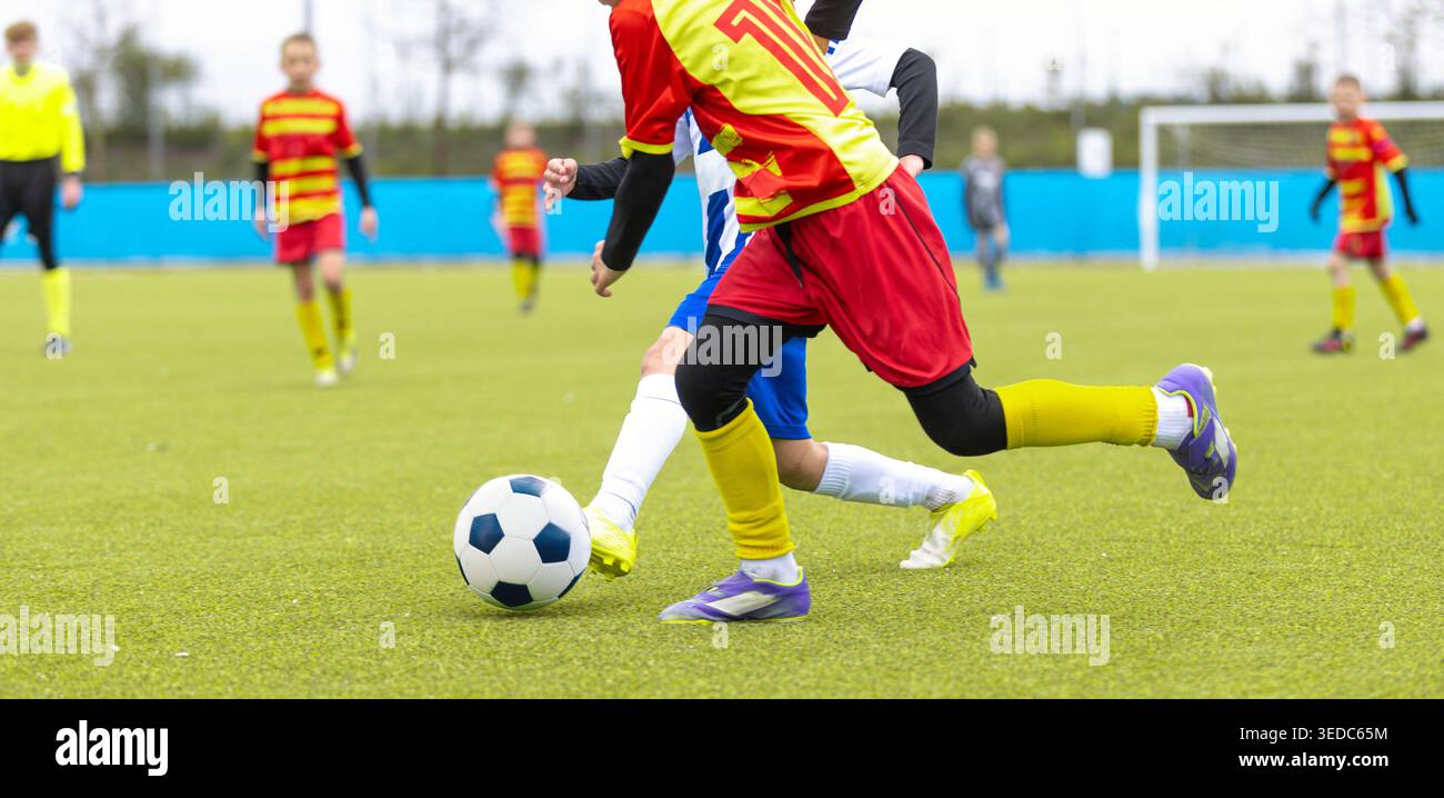 Joueur de soccer jeune dans la balle dribble uniforme rouge et jaune pendant le match de compétition sur Green Grass Field - Junior Football League action Banque D'Images
