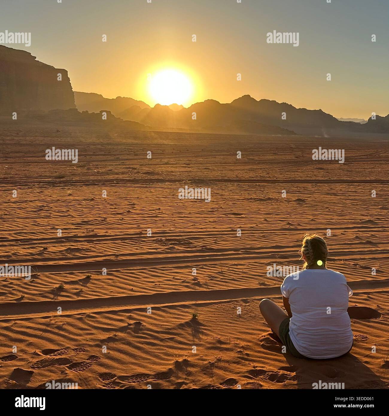 Une personne assise sur le sable du désert à Wadi Rum, Jordanie, regardant le lever du soleil sur le vaste paysage désertique. - Image de stock capturée avec un smartphone
