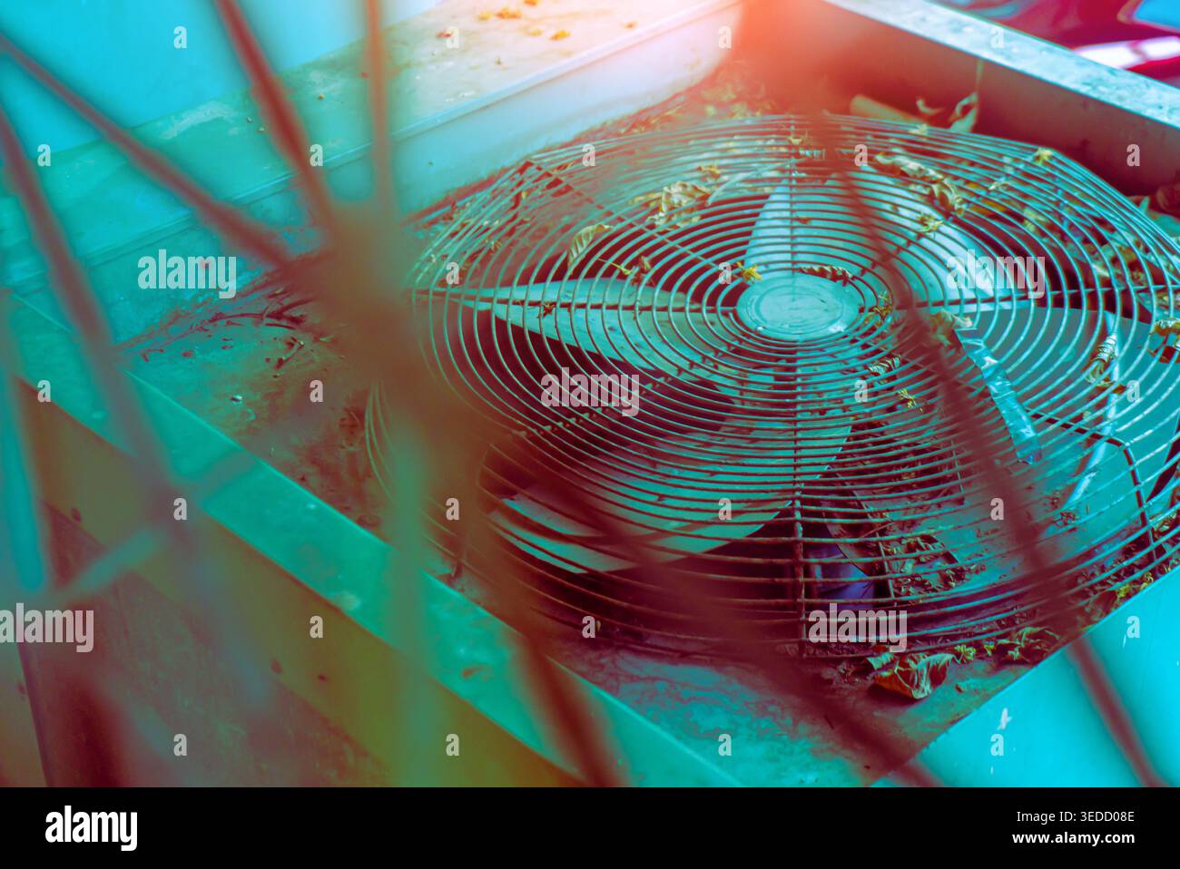 Une unité de refroidissement abandonnée présente un ventilateur poussiéreux recouvert de feuilles, sur fond bleu vif. L'image capture l'essence de la négligence et Banque D'Images