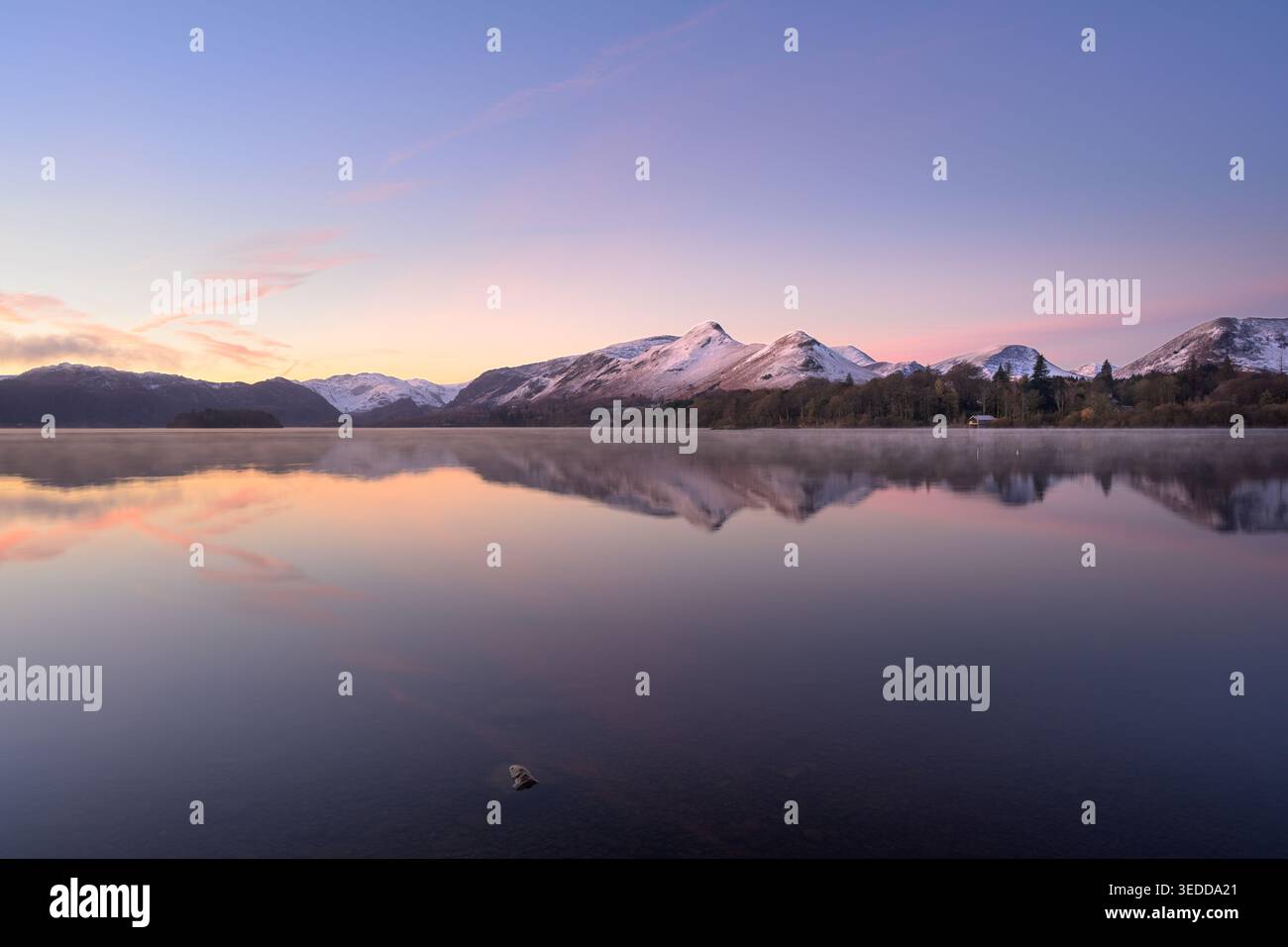 Reflets calmes d'hiver dans le lac Derwentwater au lever du soleil avec de la neige sur les montagnes, Lake District, Angleterre, Royaume-Uni. Banque D'Images
