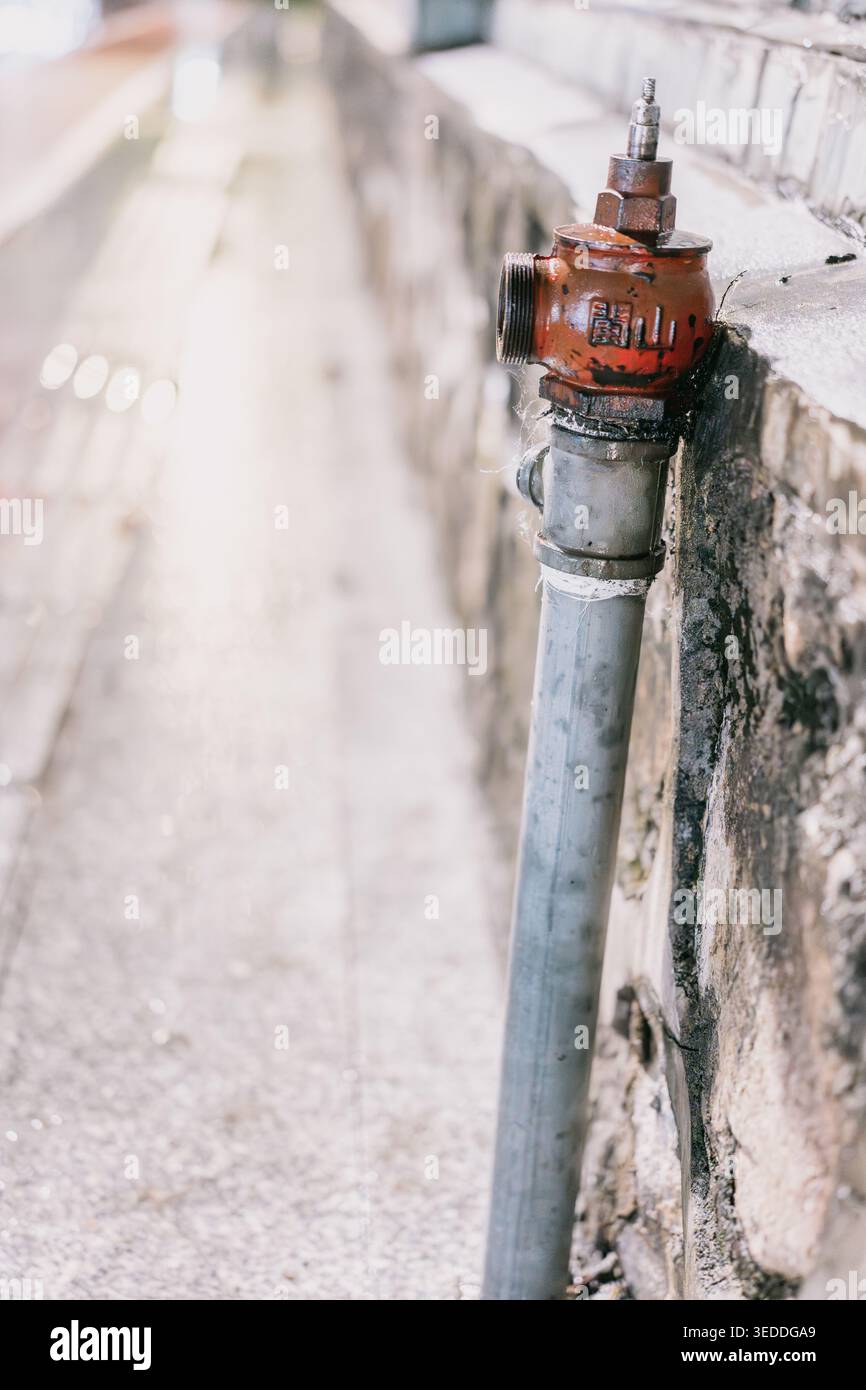 Bouche d'incendie rouge altérée montée sur un mur de béton à côté d'une ruelle pavée, faible profondeur de champ, Banque D'Images