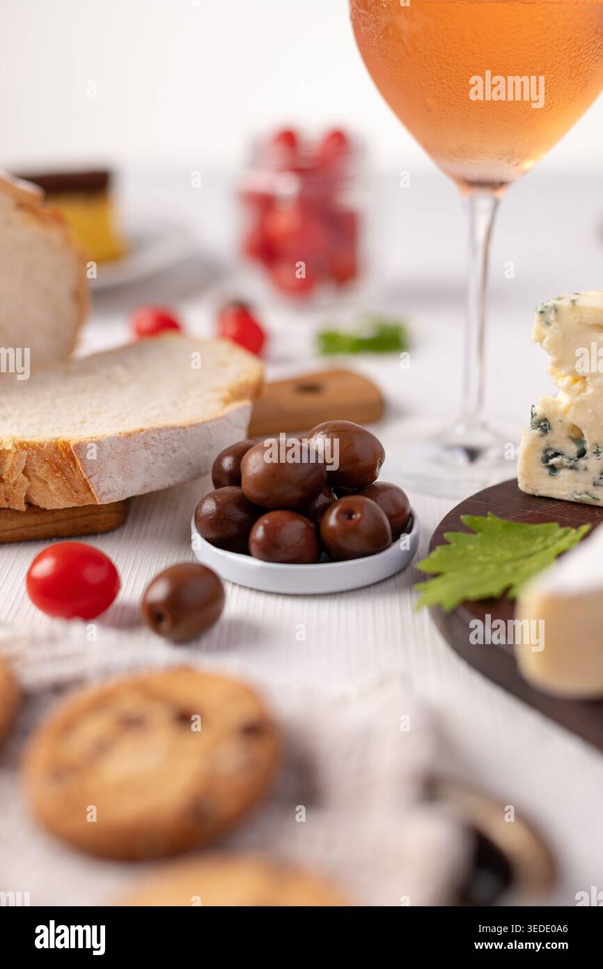 Une table est mise en place avec divers aliments et boissons. Il y a des olives dans un petit bol, du pain tranché, différents types de fromage et des biscuits. Un verre o Banque D'Images
