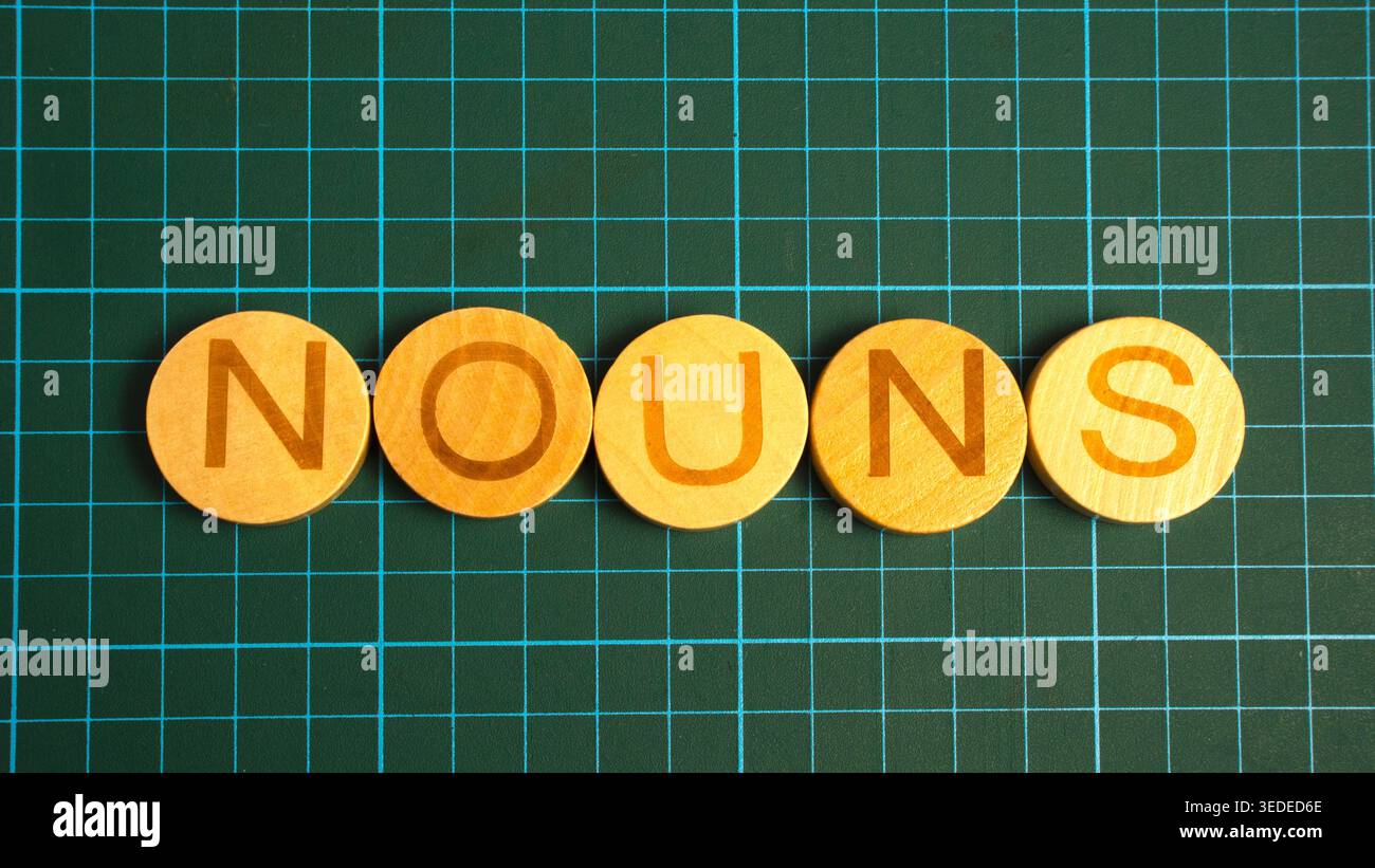 Noms texte écrit sur des carreaux de bois ronds disposés en ligne sur fond de grille verte pour l'éducation grammaticale Banque D'Images