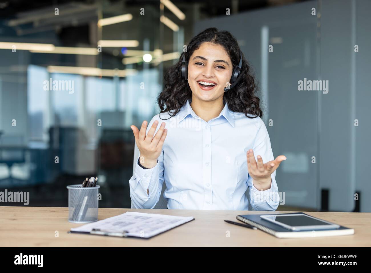 Jeune femme travaillant comme agent de centre d'appels ou représentant du service clientèle, portant un casque et souriant tout en parlant ou en présentant dans un environnement de bureau moderne Banque D'Images