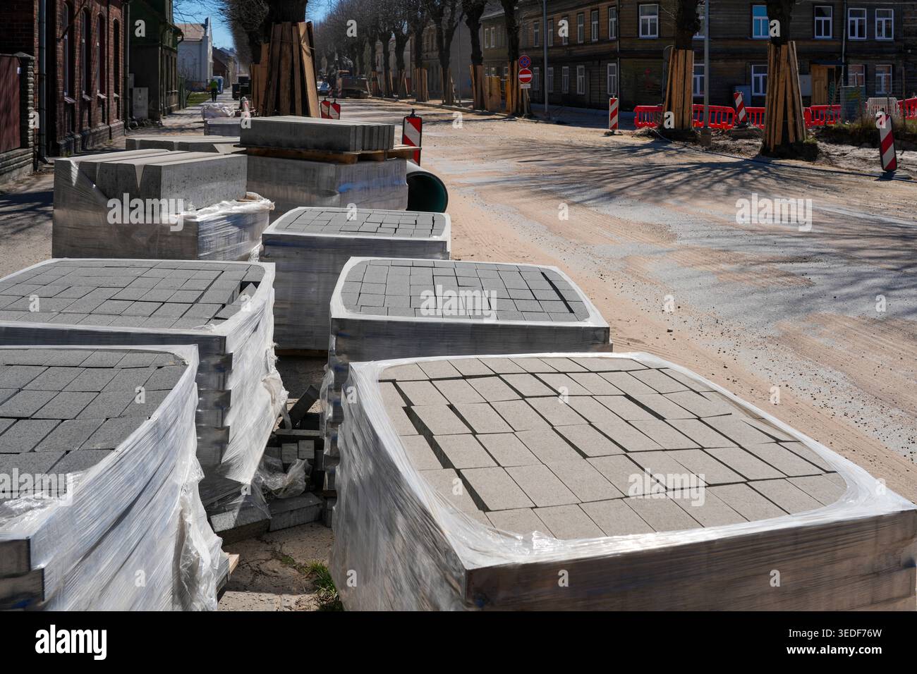 Palettes de pavés en béton enveloppés de plastique placées le long d'une rue poussiéreuse de la ville en cours de reconstruction et d'amélioration des infrastructures Banque D'Images