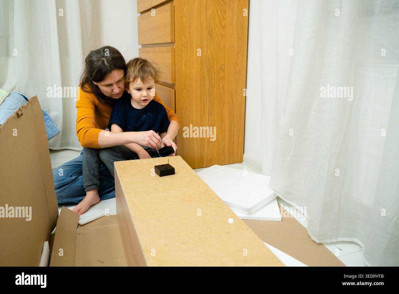 Une mère montre à son enfant comment utiliser correctement les outils et assembler une armoire. Moment éducatif sur le bricolage, la sécurité et la construction de meubles dans un environnement domestique. Banque D'Images