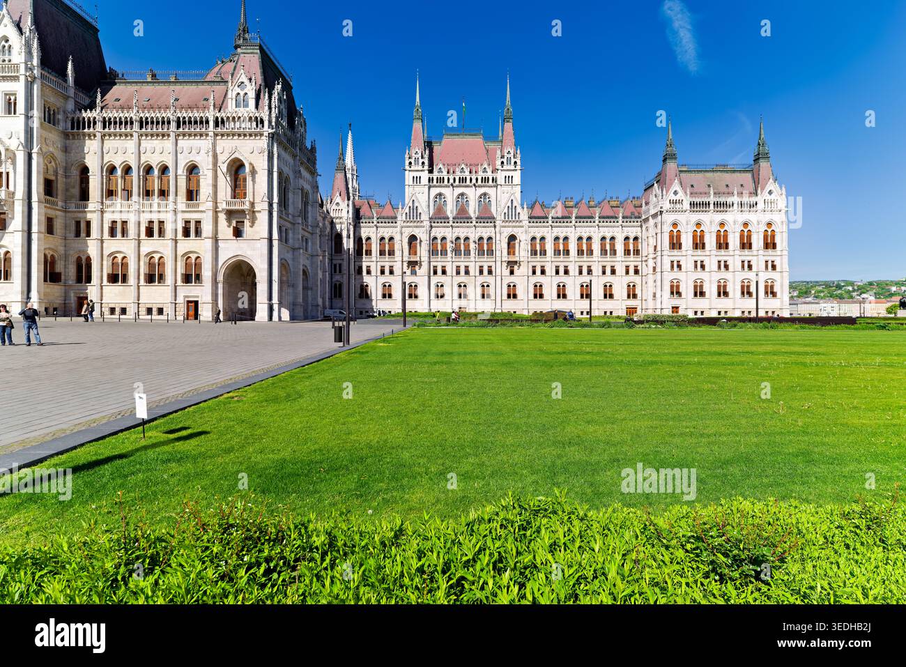 Les gens marchent près du bâtiment du Parlement à Budapest. L'herbe est verte et le ciel est dégagé. C'est une journée ensoleillée en Hongrie. Banque D'Images