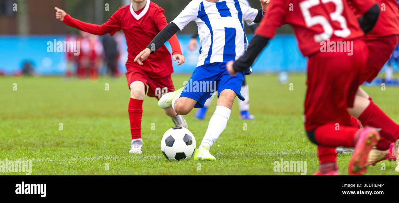 Joueurs de football junior en uniforme rouge et bleu en compétition pour la possession de ballon lors d'un match de football compétitif pour les jeunes sur le terrain Green Grass Banque D'Images