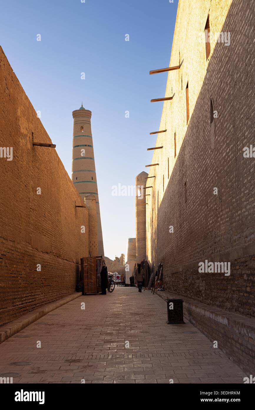 Ruelle étroite à Ichan Kala menant au minaret Islam Khodja à Khiva, Ouzbékistan. Une lumière dorée chaude illumine d'anciens murs de briques au coucher du soleil. Idéal pour les publications de voyage et le patrimoine culturel pro... Banque D'Images