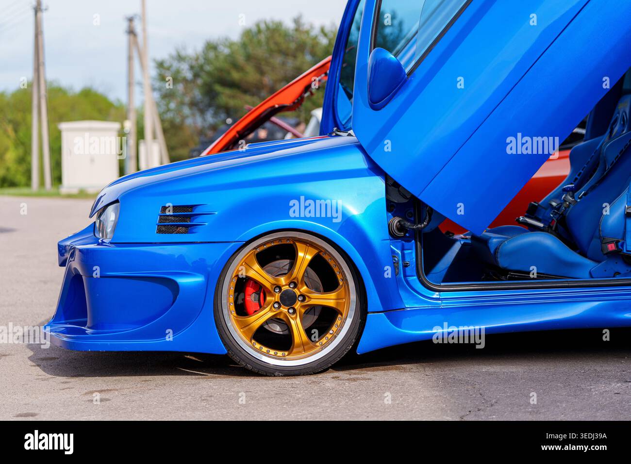 Profil latéral d'une Volkswagen Golf bleue modifiée avec portes en ciseaux verticales, jantes en alliage d'or, kit de carrosserie large, réglage automobile personnalisé et Banque D'Images
