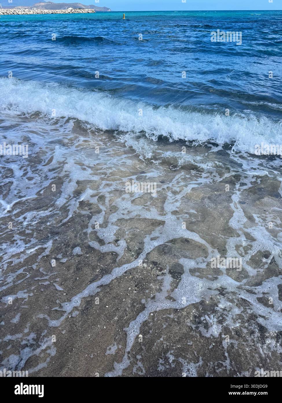 Une photo nette d'une vague turquoise transparente qui croît et se brise sur le rivage de sable sombre. - Image de stock capturée avec un smartphone