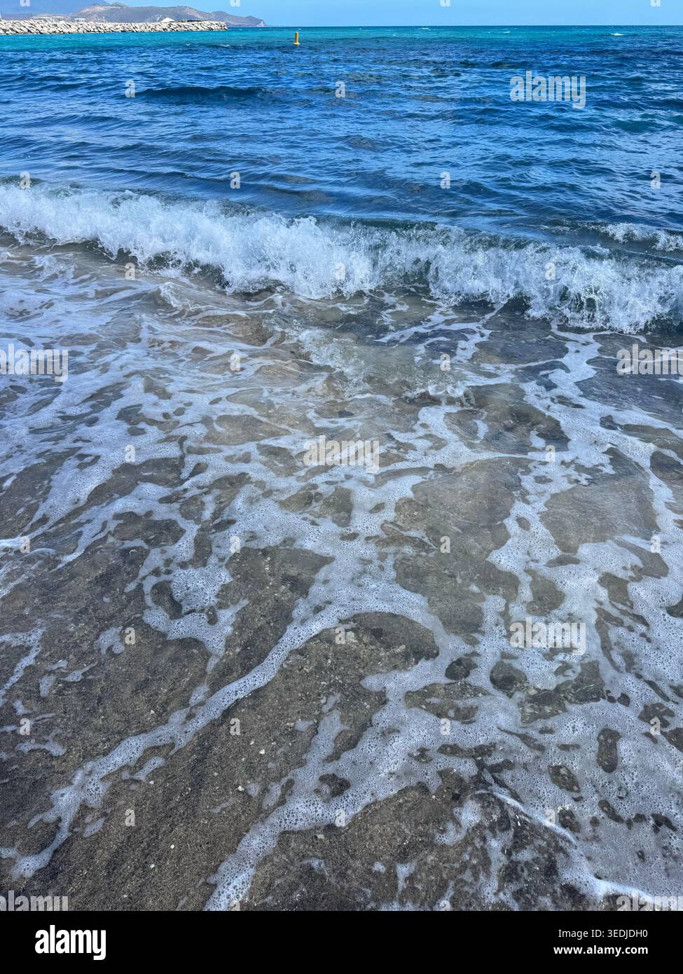Mousse blanche de vague de mer lavant sur la texture gris foncé de sable volcanique sur une plage. - Image de stock capturée avec un smartphone