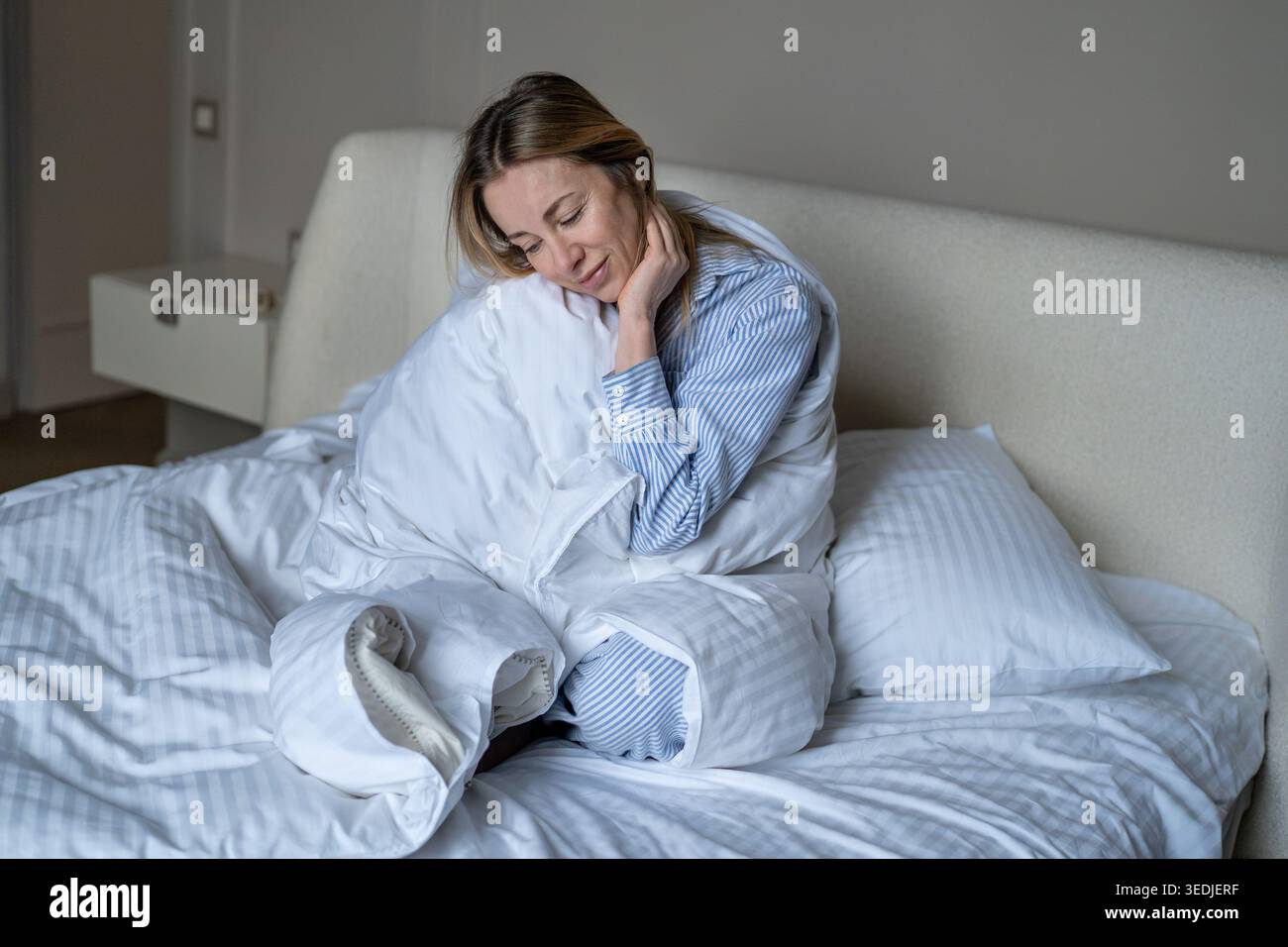 Femme heureuse appréciant la pause matinale consciente avant de commencer le jour assis couverture enveloppée assis dans le lit Banque D'Images