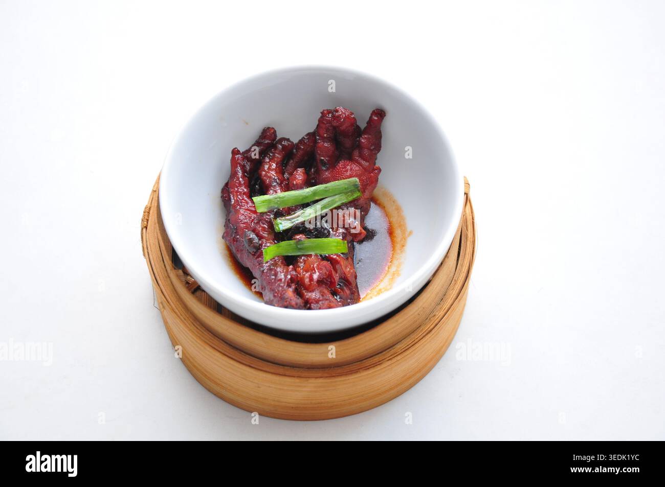 un plat traditionnel chinois à base de pieds de poulet cuits à la vapeur sucrés et salés pour un complément dimsum servi dans un bol blanc et un panier vapeur en bambou Banque D'Images