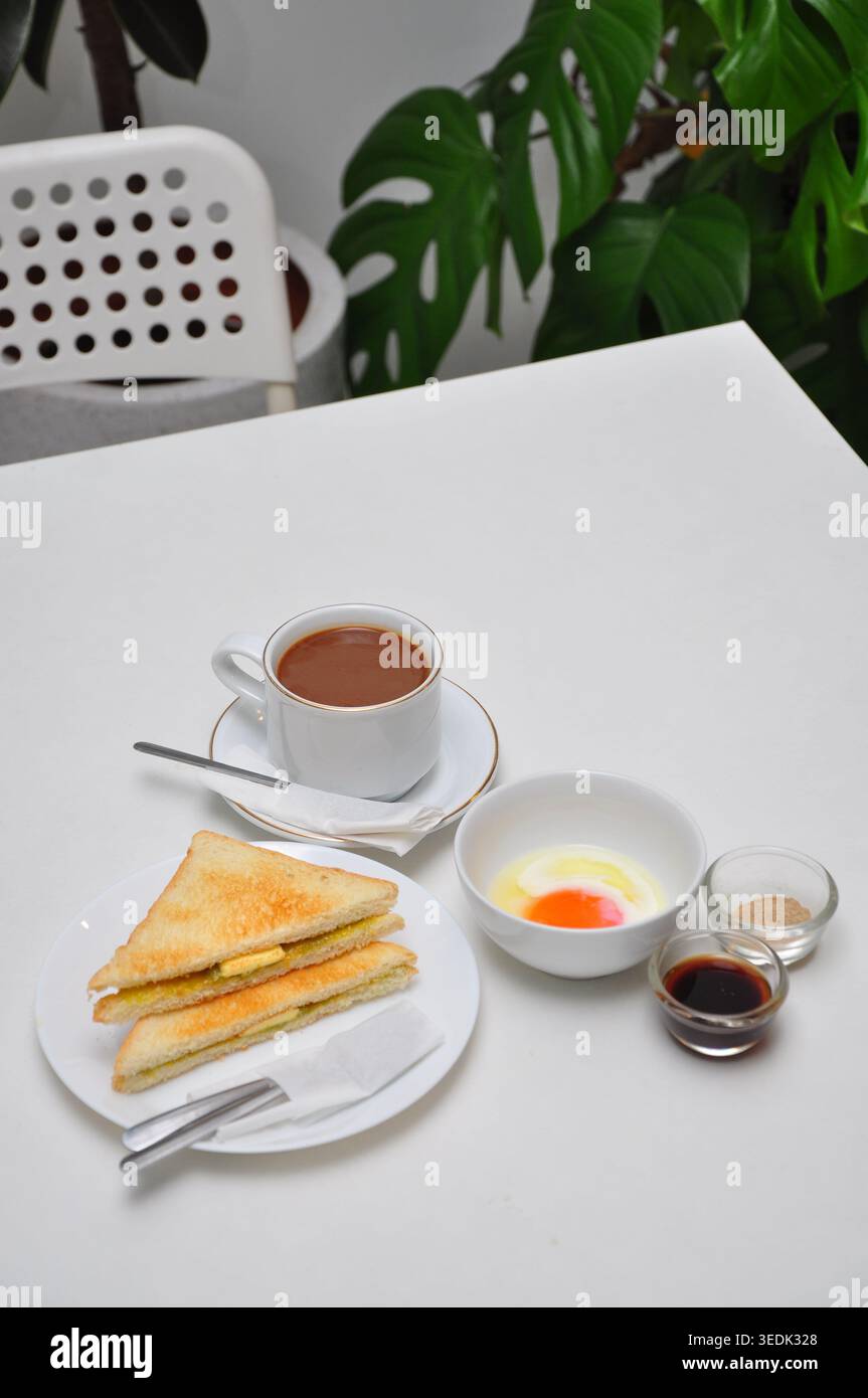 un petit-déjeuner typique de style kopitiam se compose de kopi susu ou café au lait sucré, de toasts kaya et d'œufs durs, servis dans une table blanche Banque D'Images