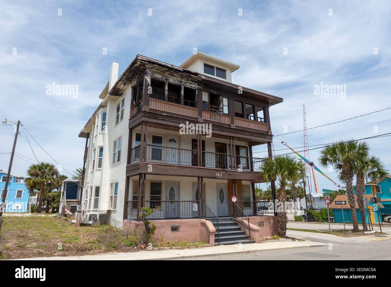 Vieille maison de plage altérée avec des palmiers et une grue arc-en-ciel en arrière-plan sous un ciel bleu à Daytona, en Floride. Banque D'Images