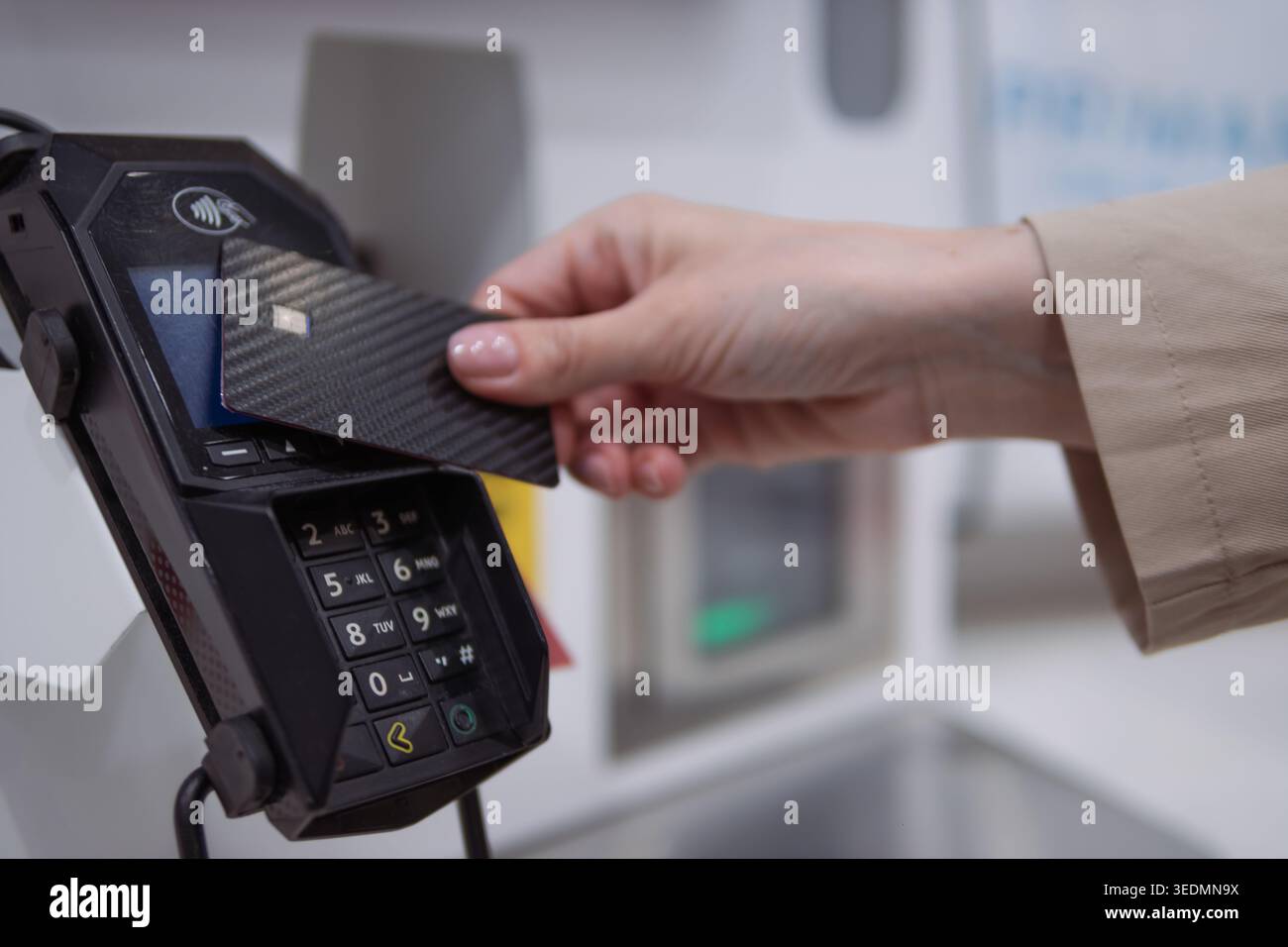 Main tenant une carte de crédit élégante en fibre de carbone tapotée contre un terminal POS pour un paiement sans contact sécurisé, illustrant le commerce de détail sans espèces moderne Banque D'Images