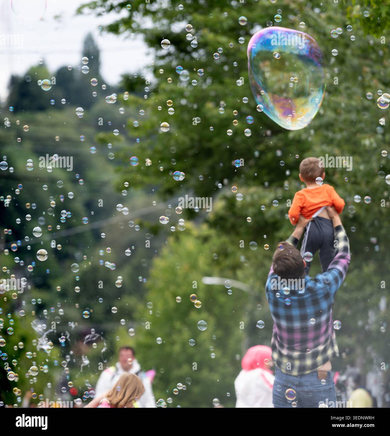Père tenant son fils vers des bulles de savon géantes pendant la Fremont Summer Solstice Fair à Seattle Banque D'Images