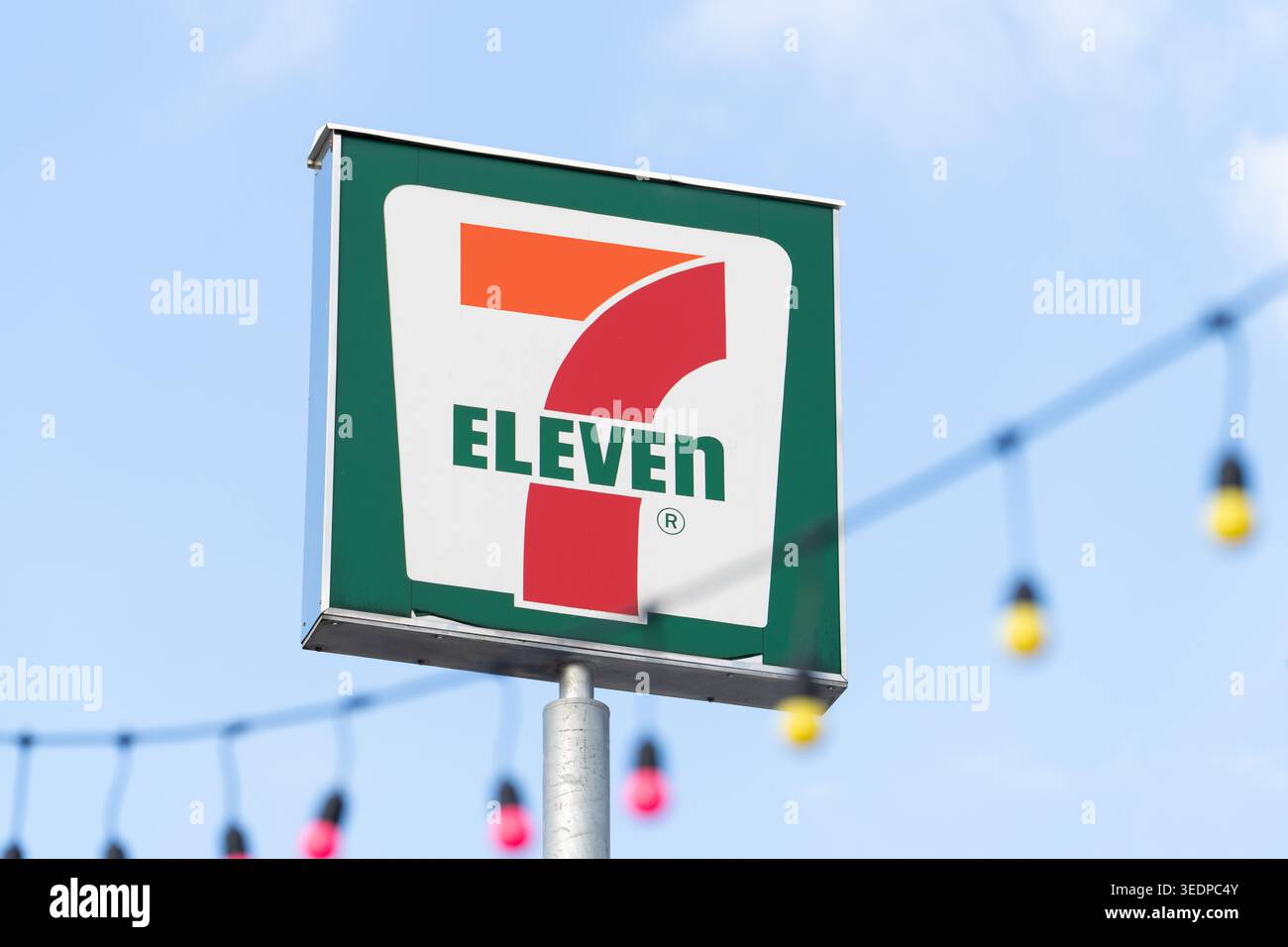 Phuket Thaïlande 29 11 2025 : 7 logo Eleven affiché sur le panneau de rue monté sur un poteau métallique contre le ciel bleu. Guirlande lumineuse décorative visible en backgro Banque D'Images