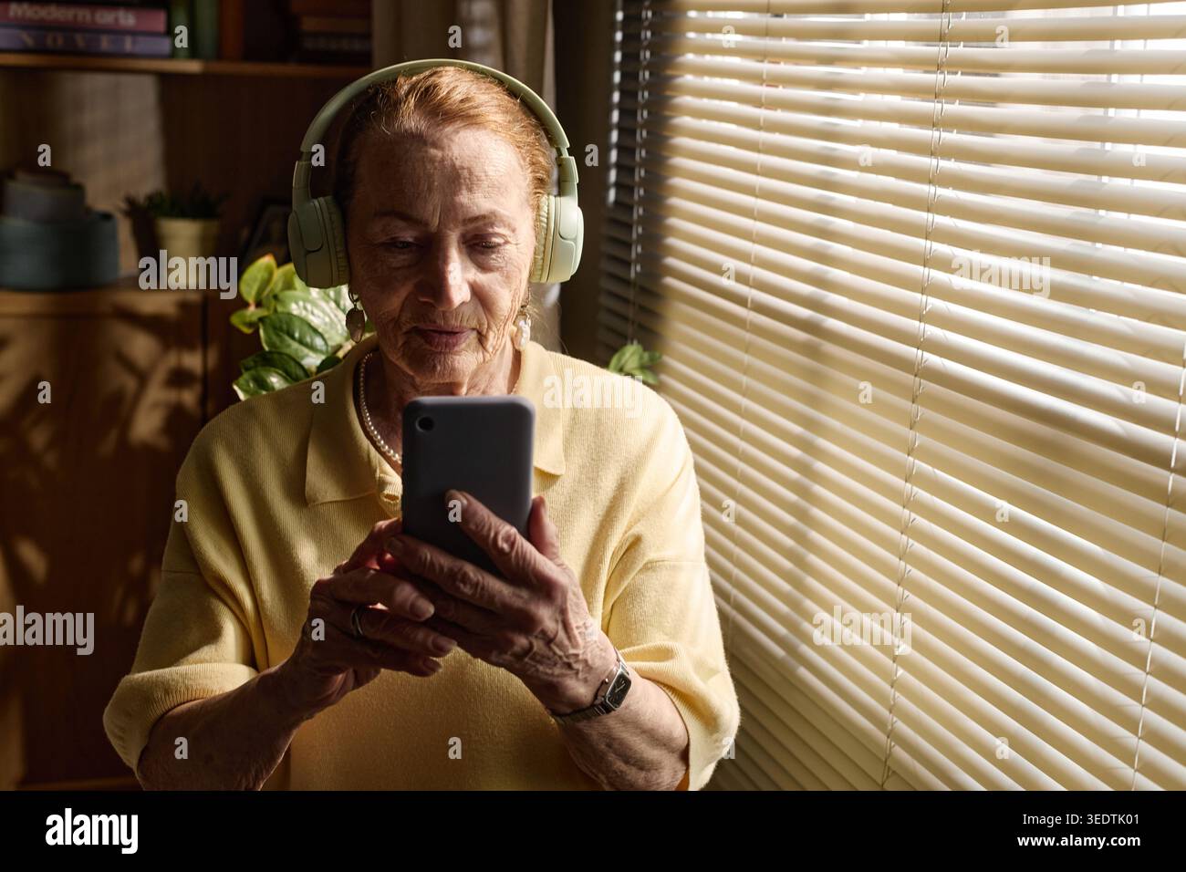 Femme senior utilisant smartphone avec casque pour appel vidéo Banque D'Images