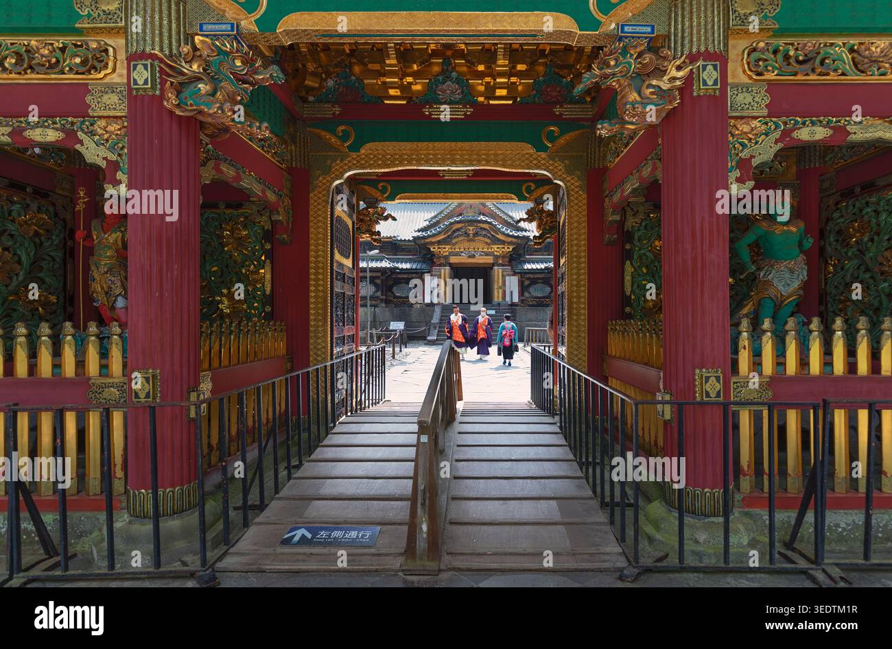 L'architecture du sanctuaire japonais richement décorée encadre une passerelle avec les visiteurs au loin dans une composition symétrique. Banque D'Images