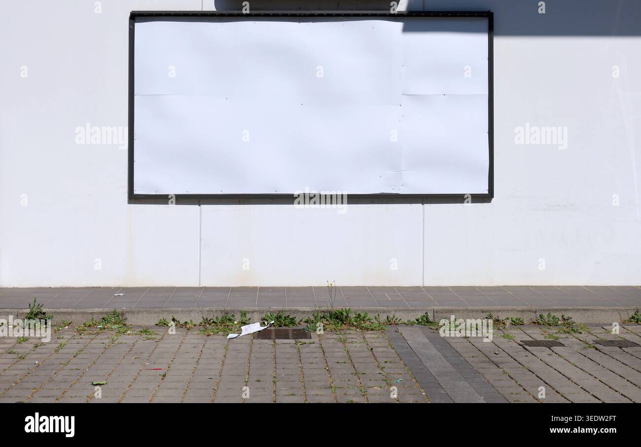 Panneau d'affichage de rue vierge au bord de la route sur le mur de béton préfabriqué blanc. Trottoir sale et rue carrelée en face. Arrière-plan pour l'espace de copie, ajoutez du texte. Banque D'Images