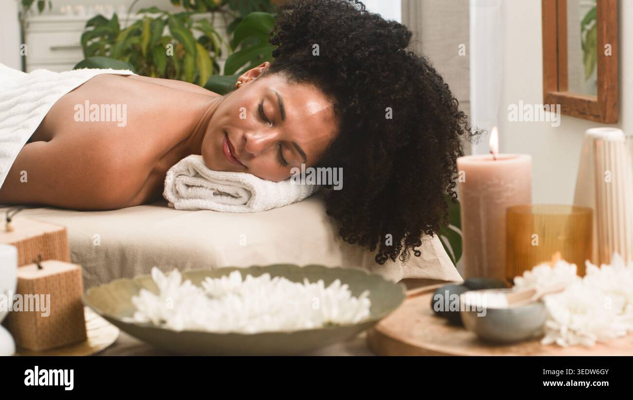 Femme détendue recevant un massage spa entouré de bougies et de fleurs dans la salle de soins tranquille Banque D'Images