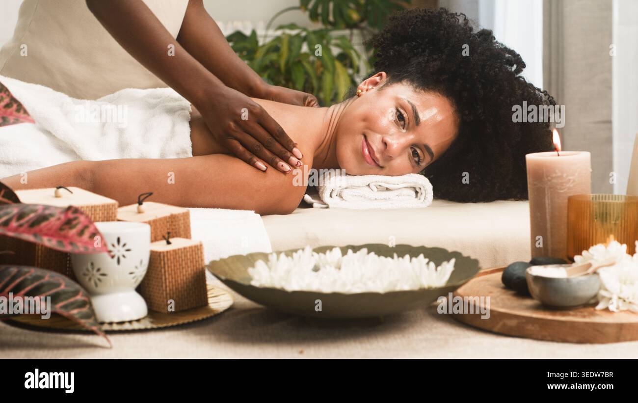 Massage spa relaxant : femme souriante recevant un massage des épaules dans un cadre de bien-être serein Banque D'Images