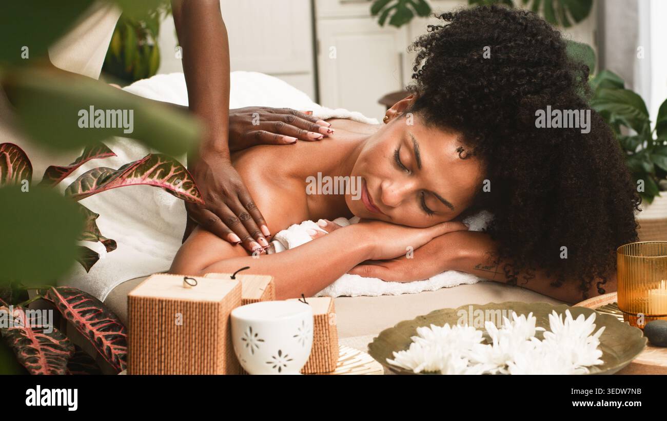 Massage relaxant du dos spa pour femme avec cheveux bouclés naturels dans un cadre de bien-être serein Banque D'Images