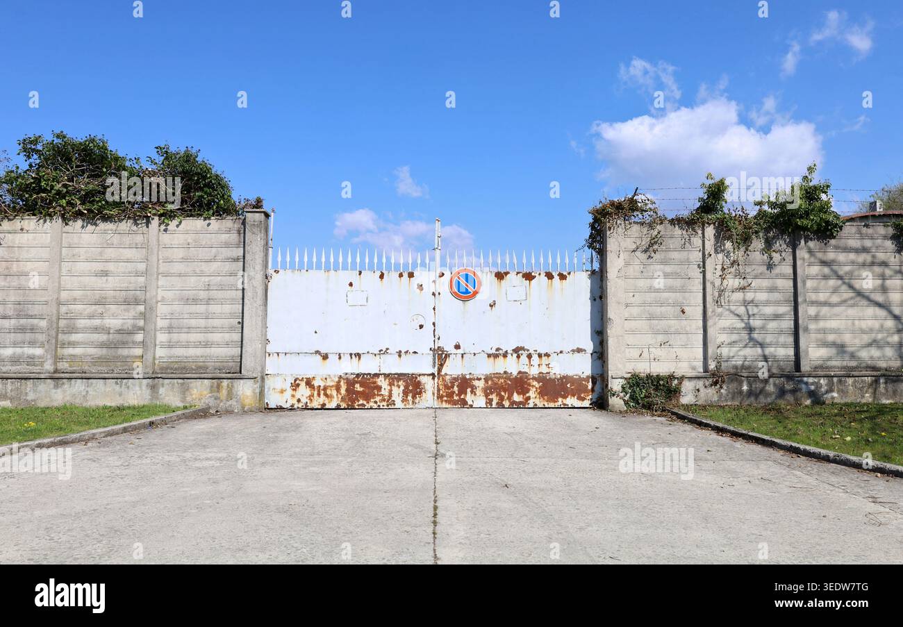 Pas de panneau d'arrêt sur une porte blanche et rouillée verrouillée avec des pointes de sécurité. Mur d'entourage en béton par les côtés, ciel au-dessus. Arrière-plan de l'espace de copie Banque D'Images