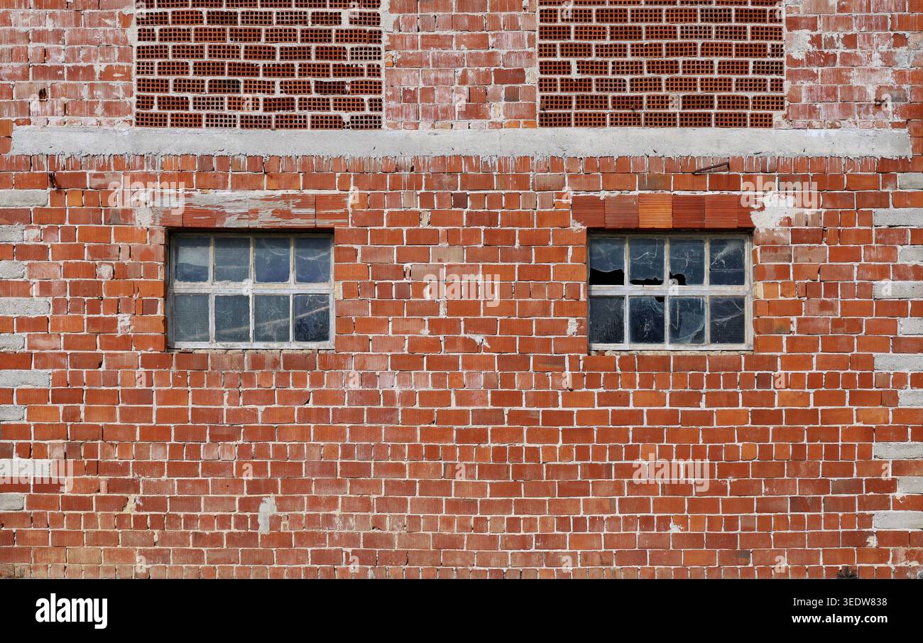 Façade en briques apparentes avec deux fenêtres endommagées d'un bâtiment industriel abandonné. Fond et texture. Banque D'Images