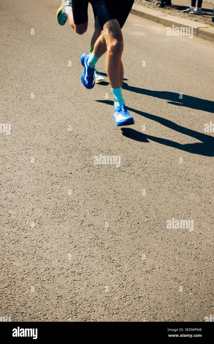 Coureurs jetant une longue ombre sur la route asphaltée pendant l'entraînement en plein air en plein soleil, concept de fitness Banque D'Images