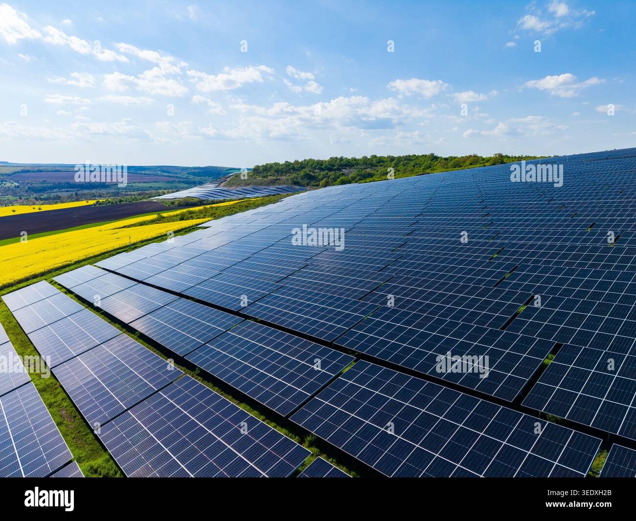 Les panneaux solaires couvrent un vaste champ avec une colline verte en arrière-plan. Le ciel est clair et lumineux avec quelques nuages visibles. La scène montre renouvelable Banque D'Images